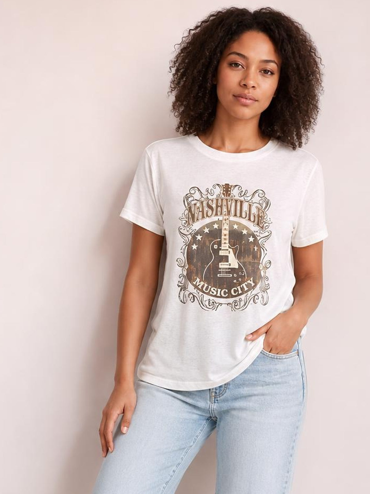 Model wears a white guitar graphic round neck short sleeve T-shirt with a relaxed silhouette, standing casually with one hand in her jeans pocket.