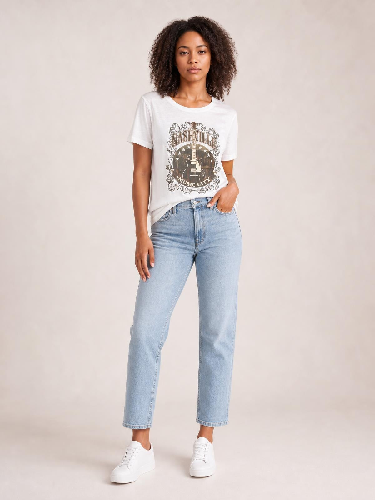 Model wearing a white guitar graphic round neck short sleeve T-shirt with a relaxed straight silhouette, paired with light-wash jeans and one hand in her pocket.
