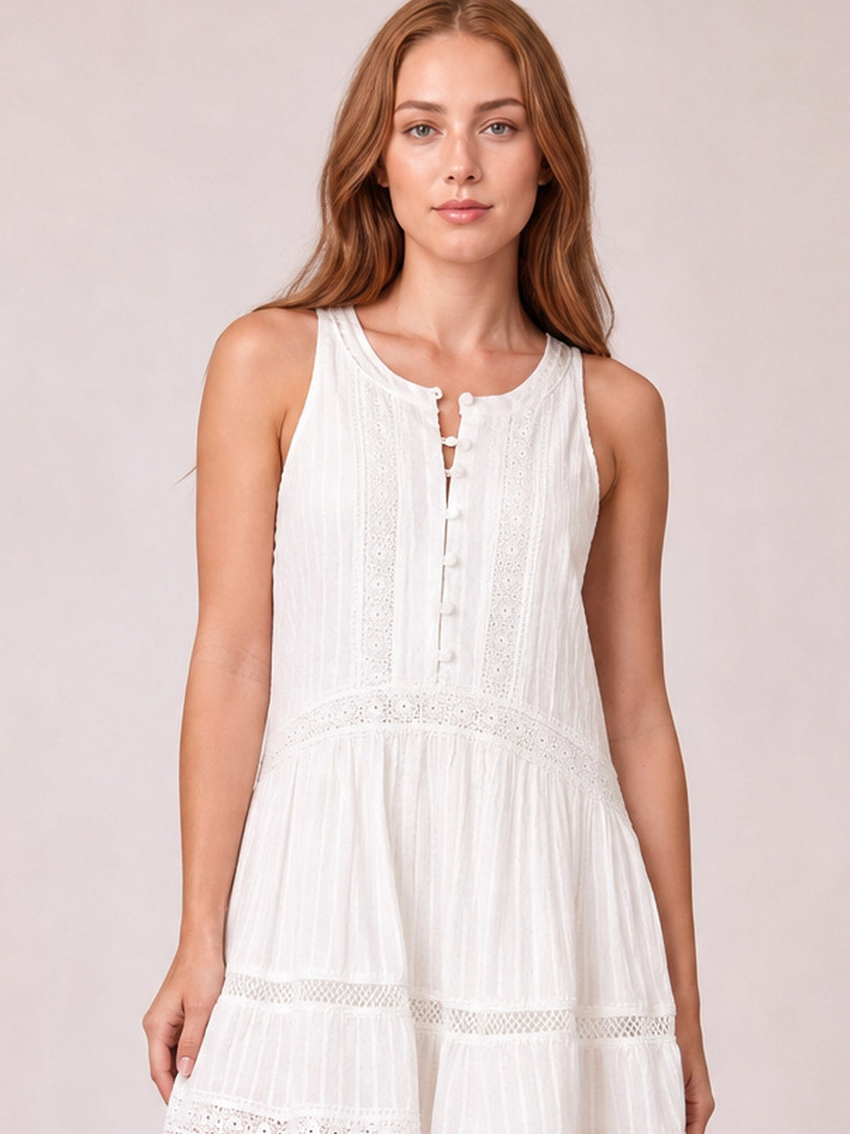 Model standing with arms at her sides wears a white sleeveless mini dress with a half-button front, lace bodice panels, defined waist, and gently flared tiered skirt.