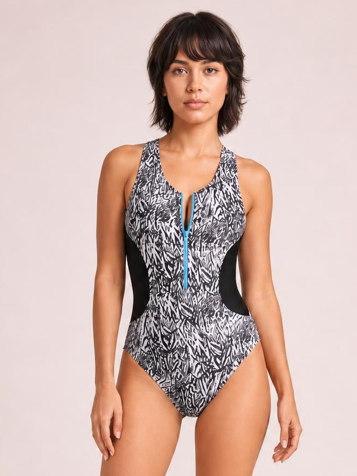 Model poses front-facing in a black-and-white printed one-piece swimsuit with a racerback-style cut, contrasting black side panels, and a half zip neckline.
