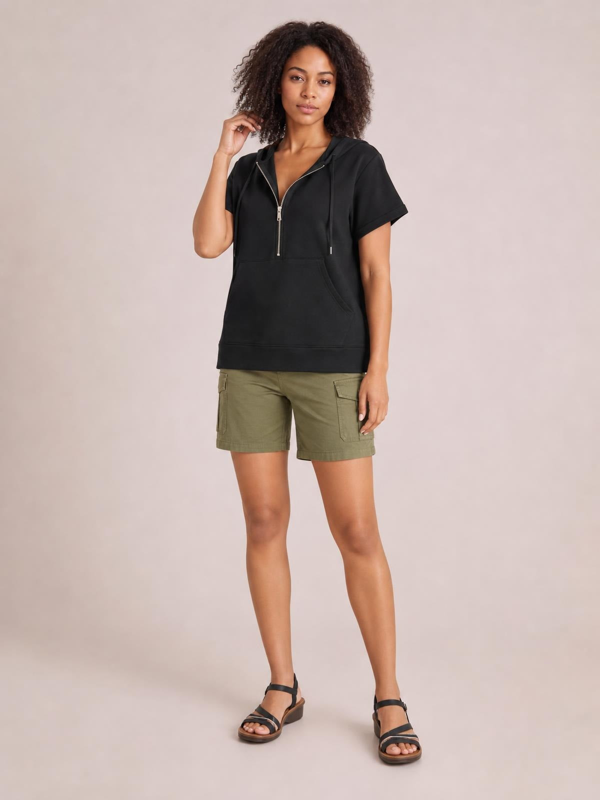 Model wearing a black short-sleeve hooded top with a half zip, relaxed silhouette, drawstring hood, and spacious front kangaroo pocket.