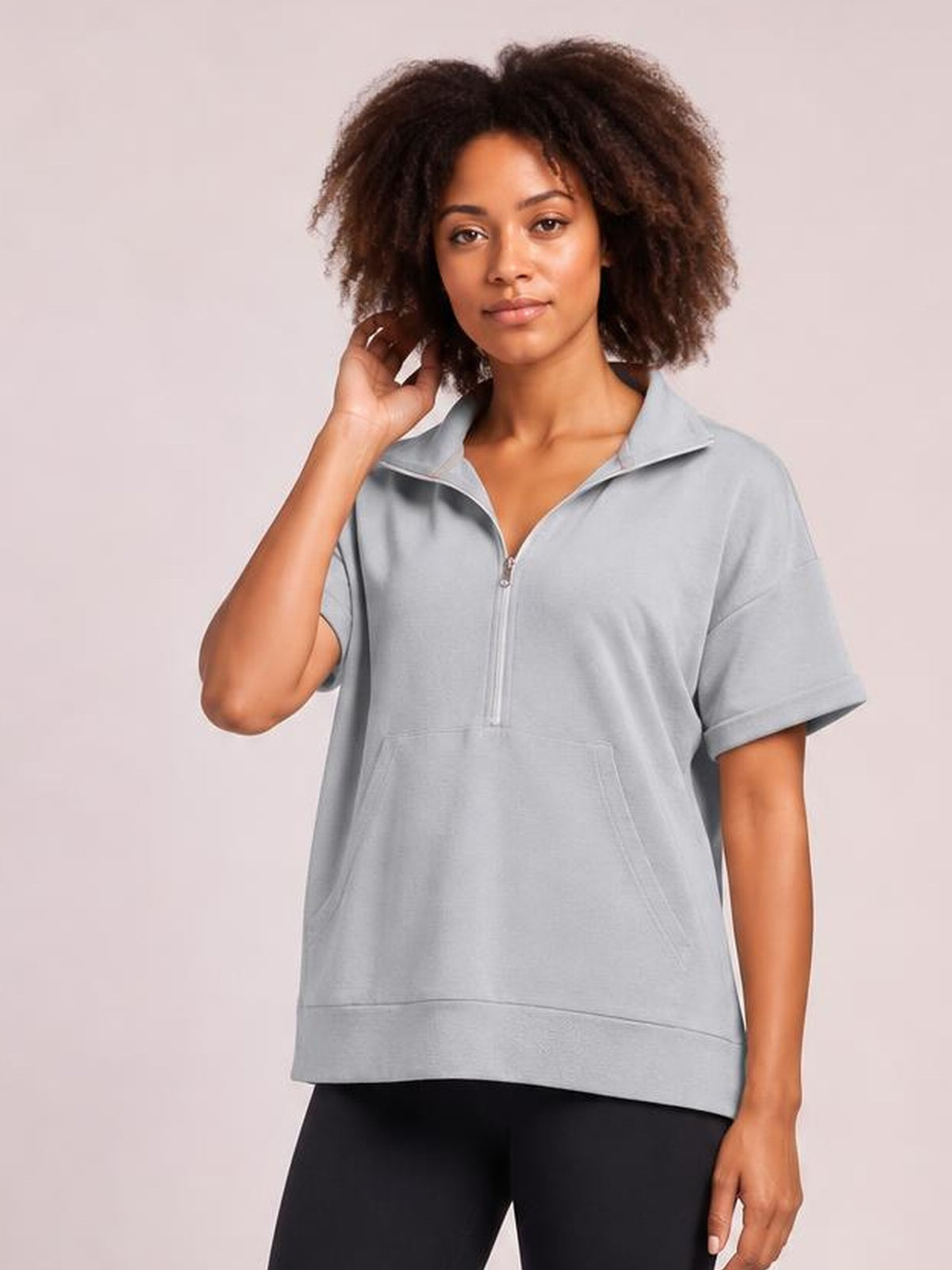 Model wearing a light gray short-sleeve hooded top with a half-zip collar, relaxed silhouette, and front kangaroo pocket.