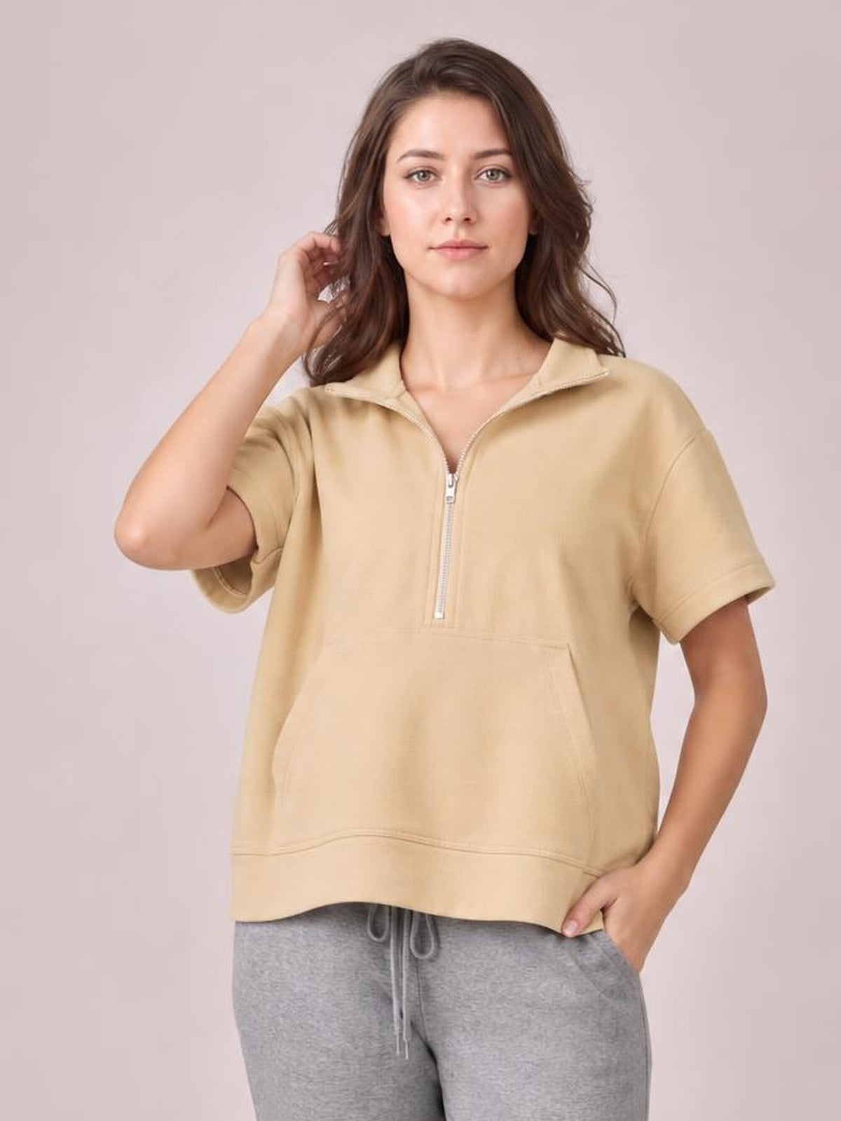 A model poses in a tan half-zip short-sleeve hooded top with a relaxed silhouette, ribbed trim, and a roomy front kangaroo pocket.