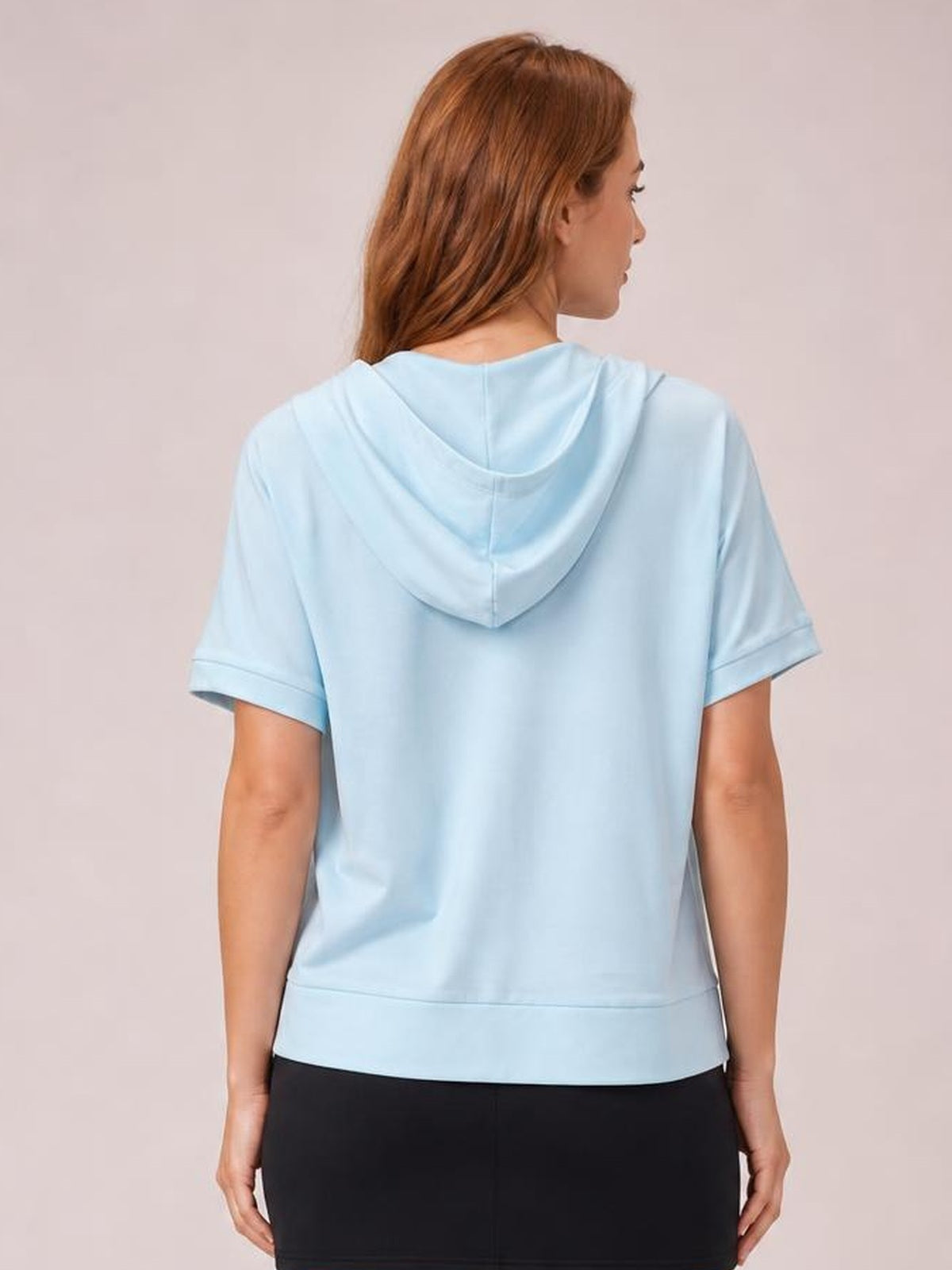 Model stands facing away in a light blue short-sleeve hooded top with a relaxed silhouette, draped hood, cuffed sleeves, and straight hem.
