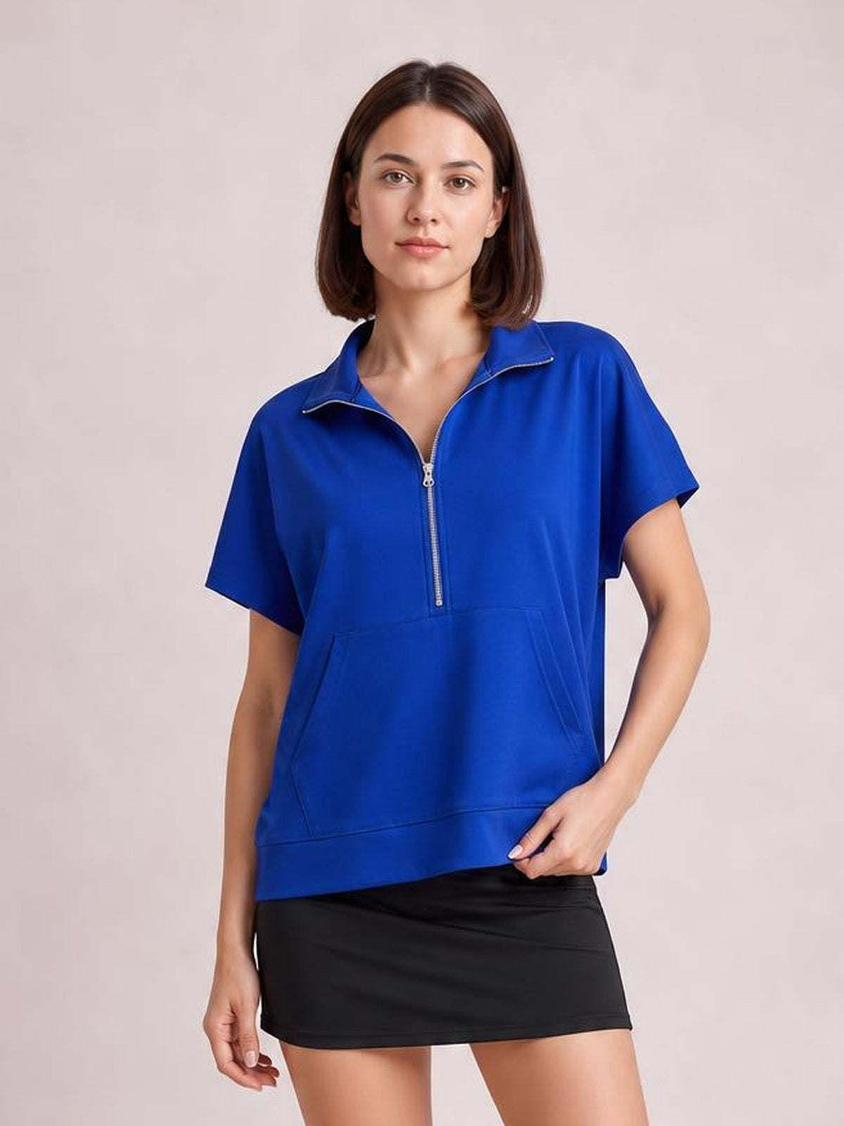 A woman poses in a vibrant blue short-sleeve hooded top with a half-zip front, relaxed silhouette, and spacious kangaroo pocket.