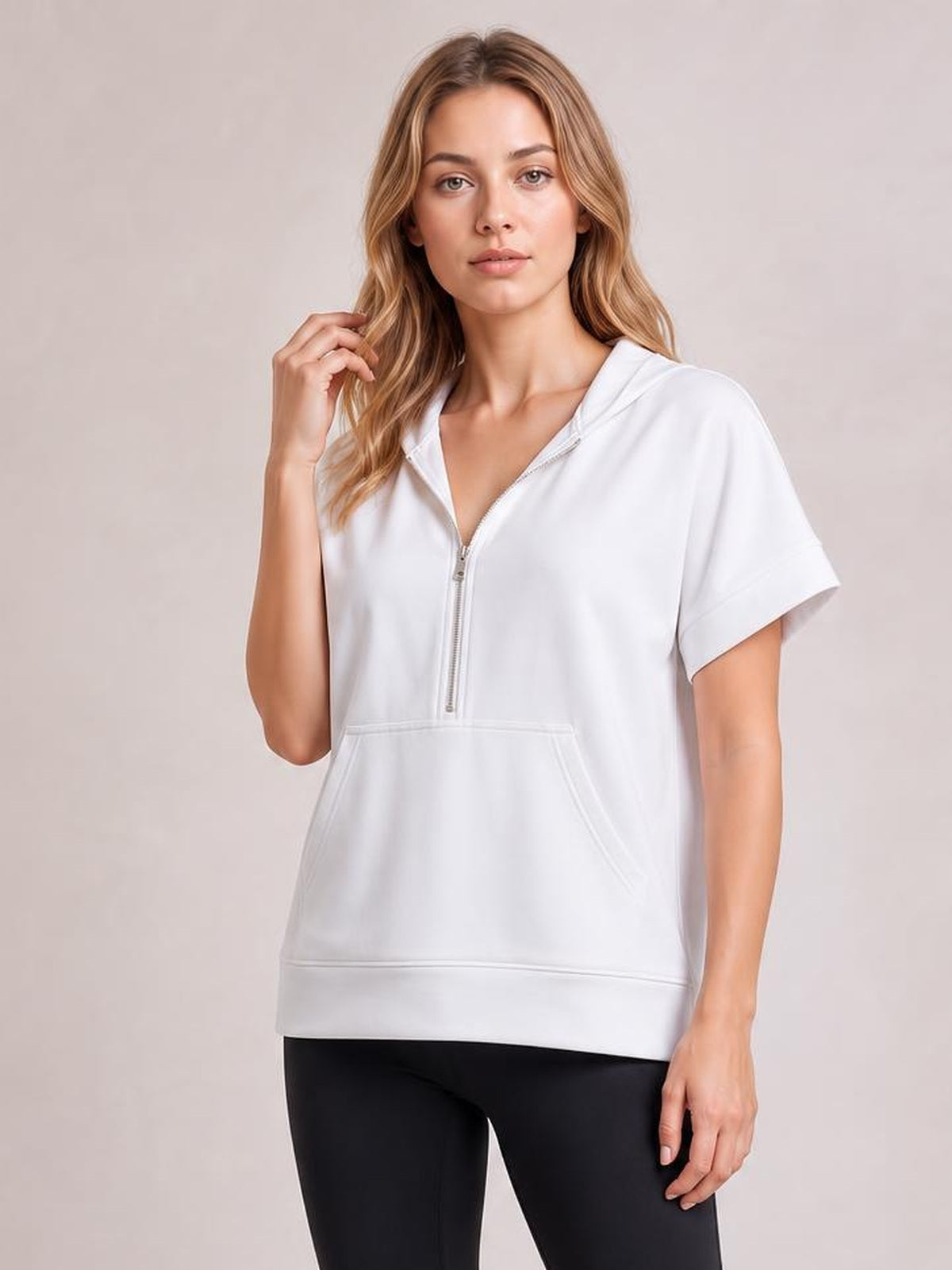 Model poses in a white short-sleeve hooded top with a half zip, kangaroo pocket, relaxed silhouette, and wide ribbed hem.