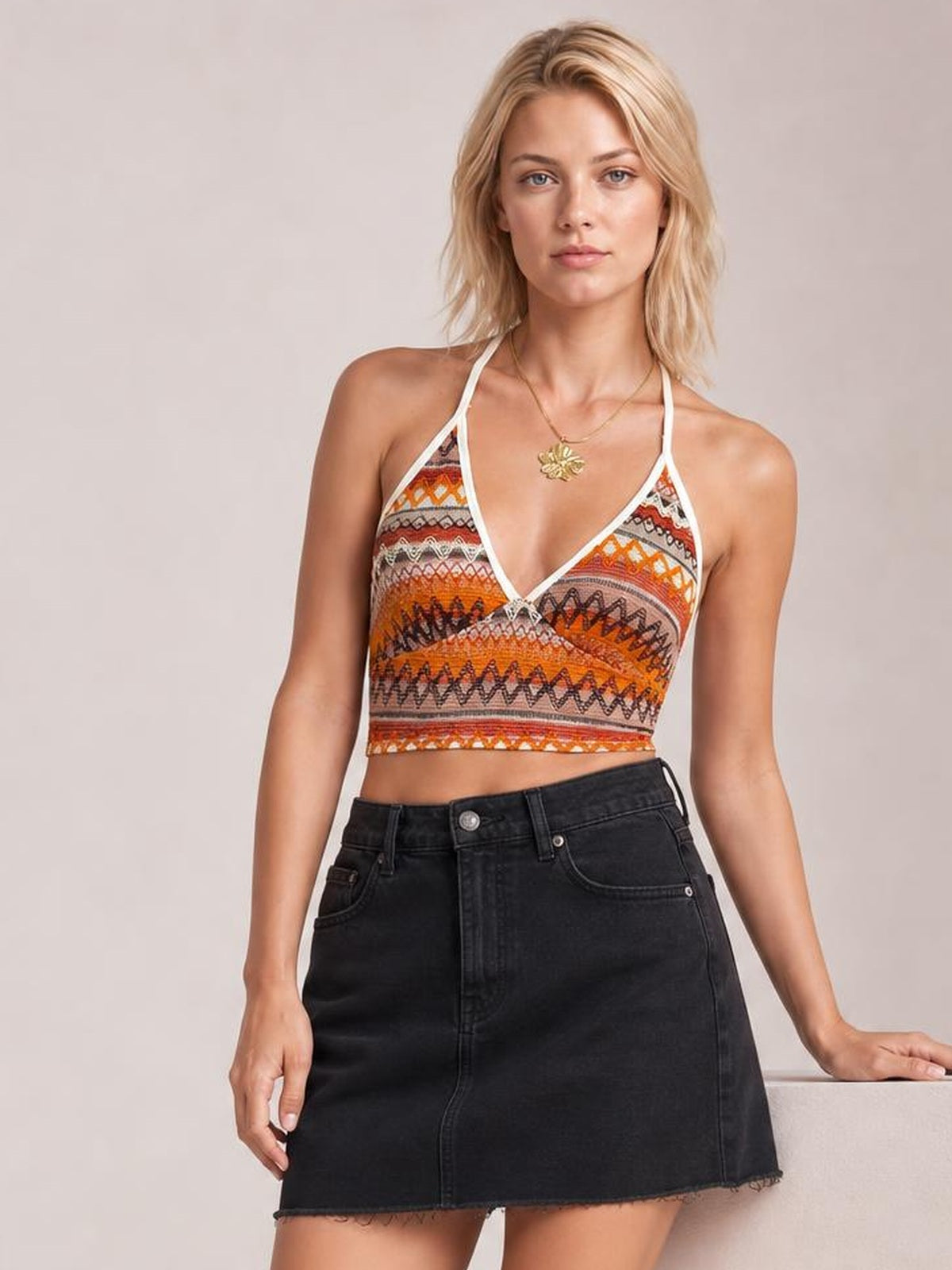 Model wearing a multicolored geometric halter neck short cami with white trim, tie detail, V-neckline, fitted cropped silhouette, and thin straps.