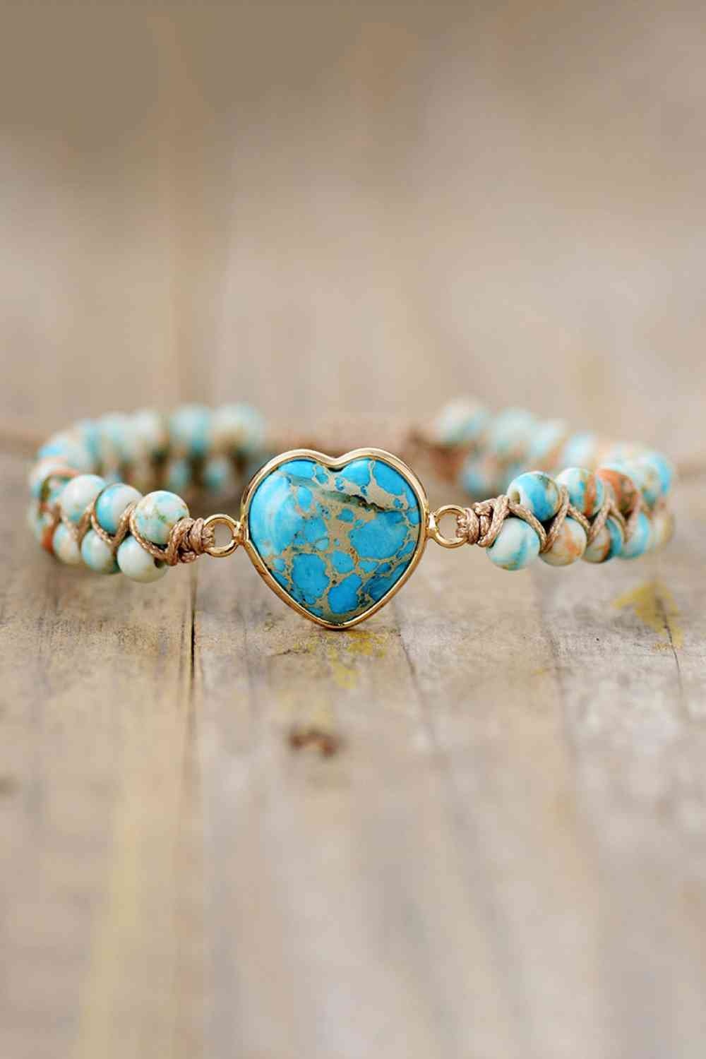 A handmade heart-shape natural stone bracelet features turquoise and cream beads, a marbled blue heart centerpiece, and copper-tone links with braided cord construction.
