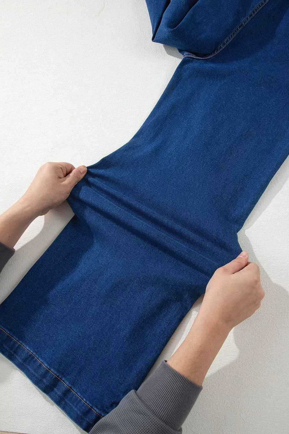 Dark blue wide-leg jeans are laid flat as hands gently stretch the leg, highlighting the slightly stretchy denim, broad silhouette, and stitched seams.