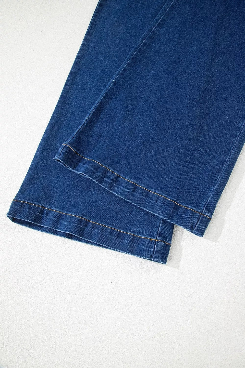 Close-up of dark blue wide-leg jeans showing stitched leg seams, structured hems, and subtle fading along the folded lower edges.