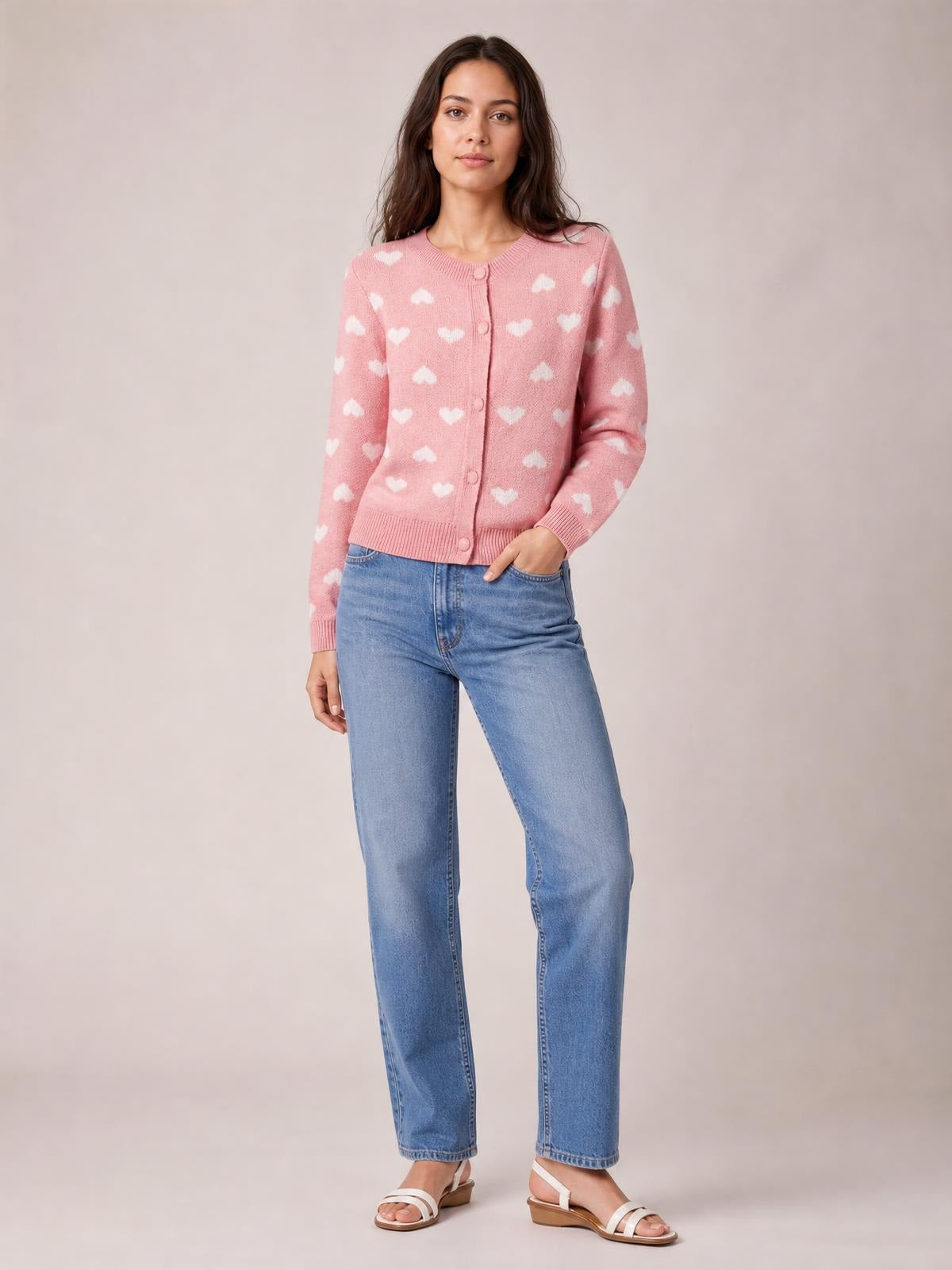 Model poses in a pink heart-pattern button-front cardigan with ribbed trim, long sleeves, and a relaxed silhouette over light-wash jeans.