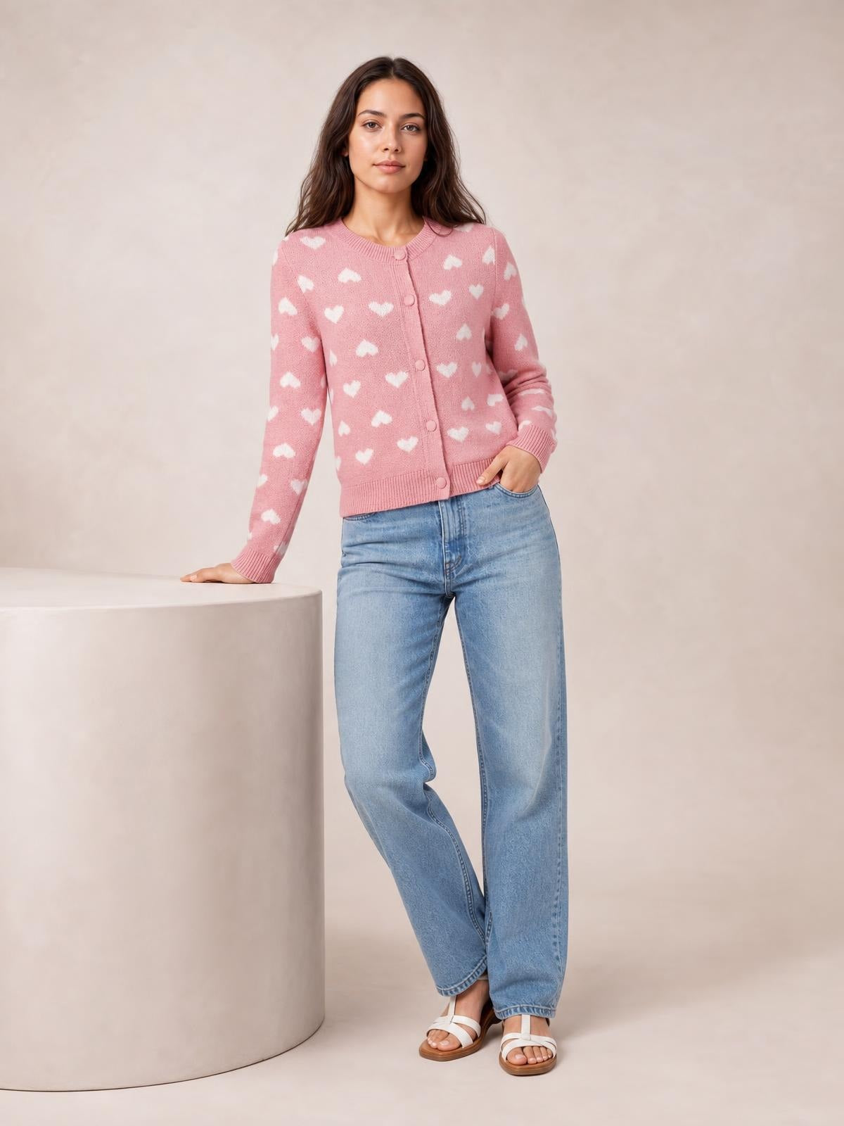 A model poses in a pink heart pattern button-front cardigan with long sleeves, ribbed trim, and a gently fitted silhouette.