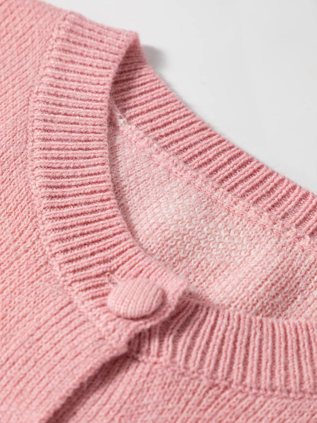 Close-up of a pink knitted cardigan showing the ribbed button-front construction, textured weave, and a visible matching button.