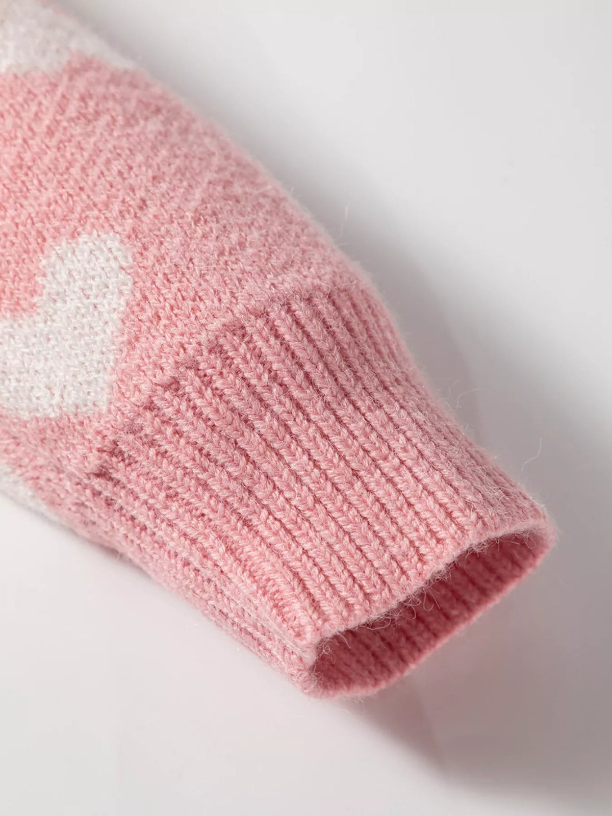 Close-up of a pink ribbed knit cardigan sleeve cuff showing a soft textured construction and part of a white heart pattern.