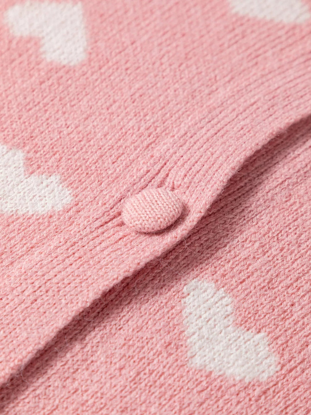 Close-up of a pink knit button-front cardigan featuring a white heart pattern, soft textured construction, and a matching pink button.