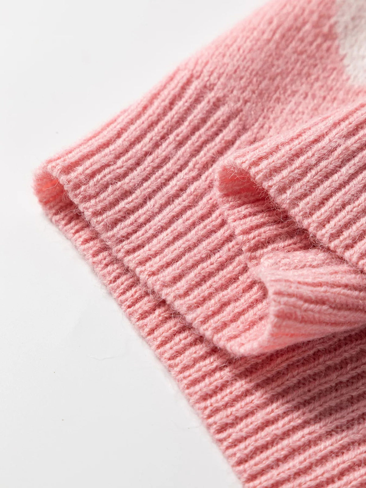 Close-up of soft pink cardigan knit fabric showing fine ribbed construction, fuzzy texture, and a folded garment edge.
