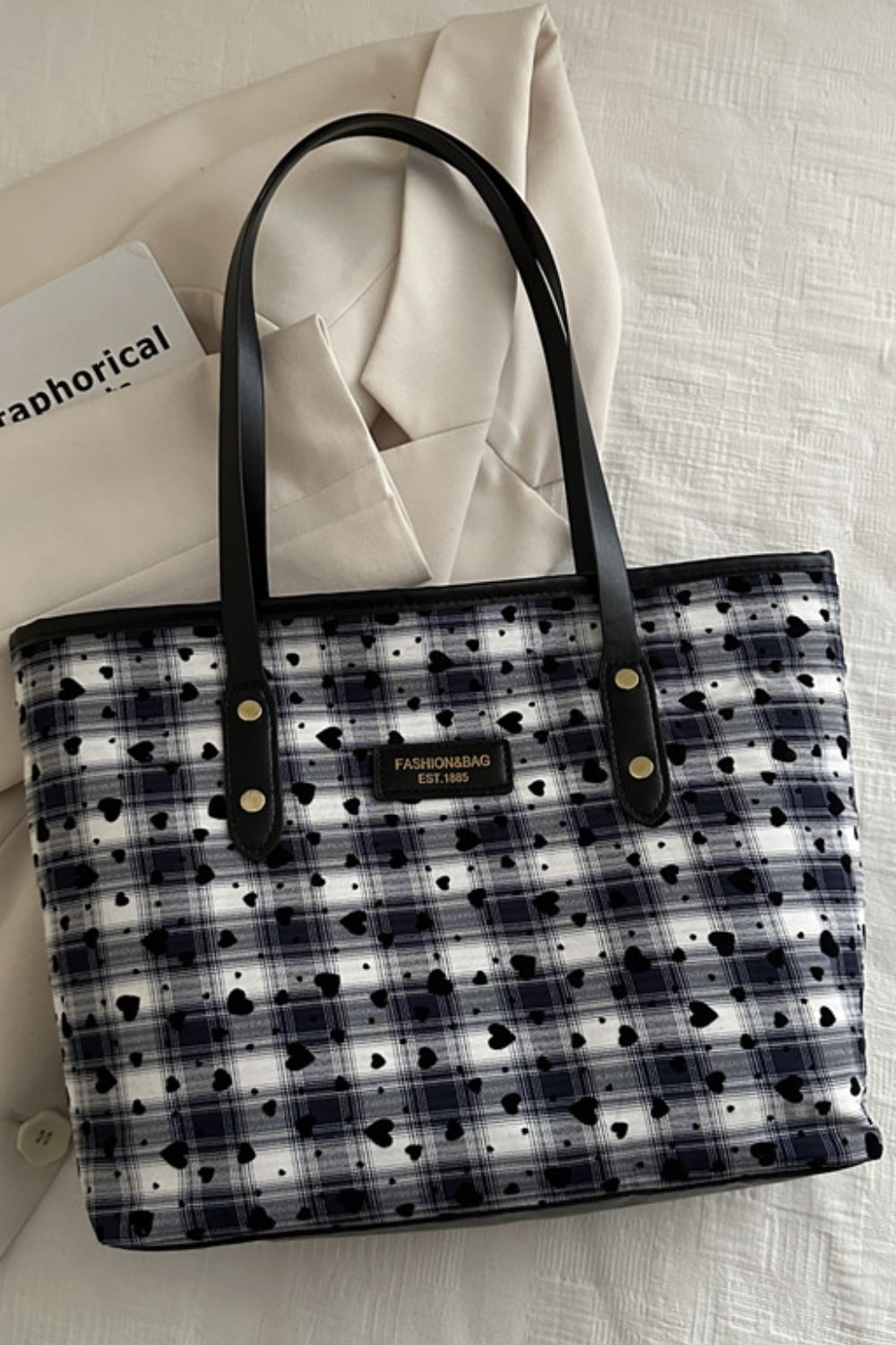 A medium heart plaid tote bag features a structured canvas body, black PU leather shoulder straps, and a zip-top closure in a roomy rectangular silhouette.