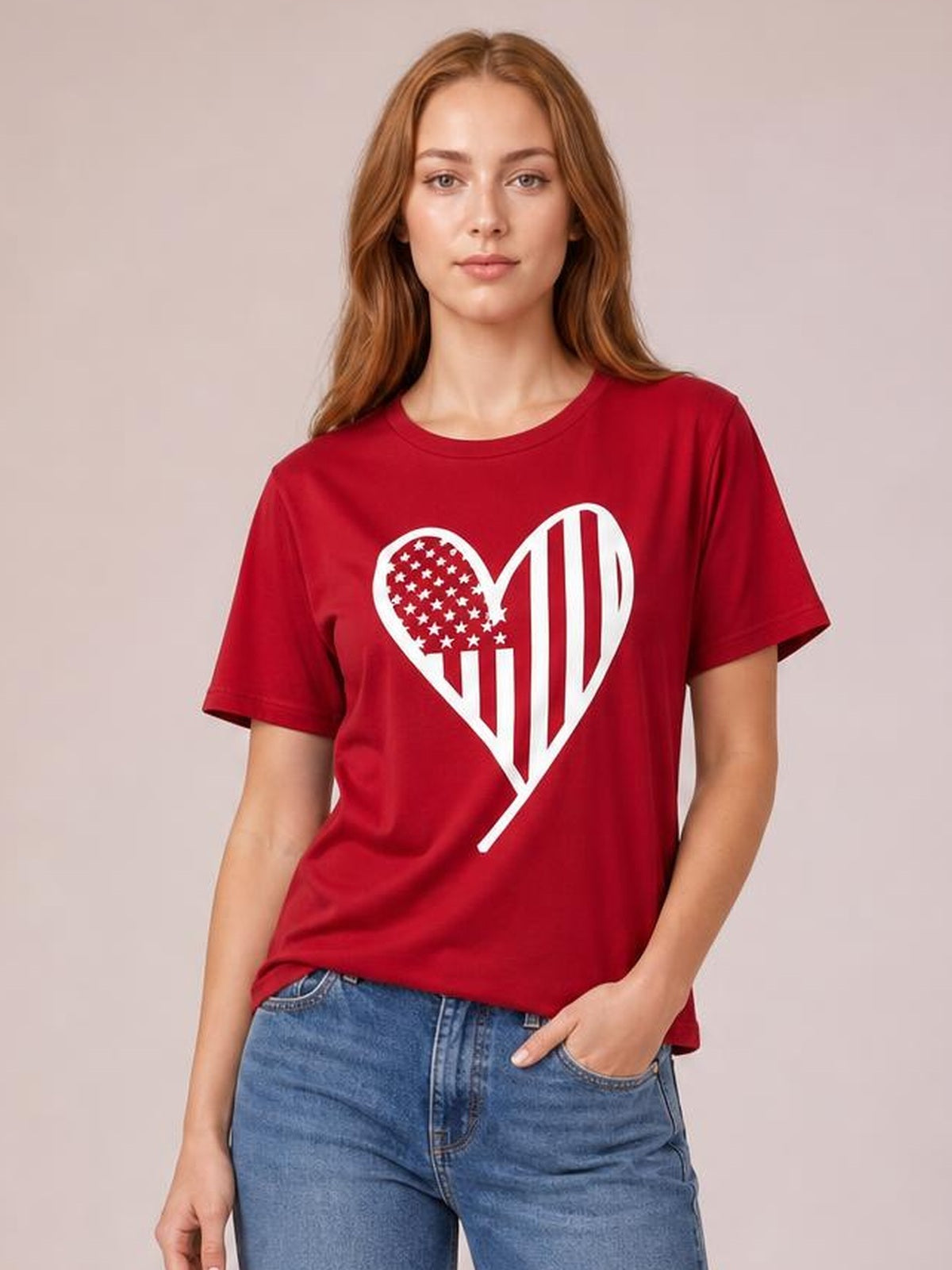 Model wearing a red heart round neck short sleeve T-shirt with a bold white heart graphic, relaxed silhouette, and one hand in her jeans pocket.