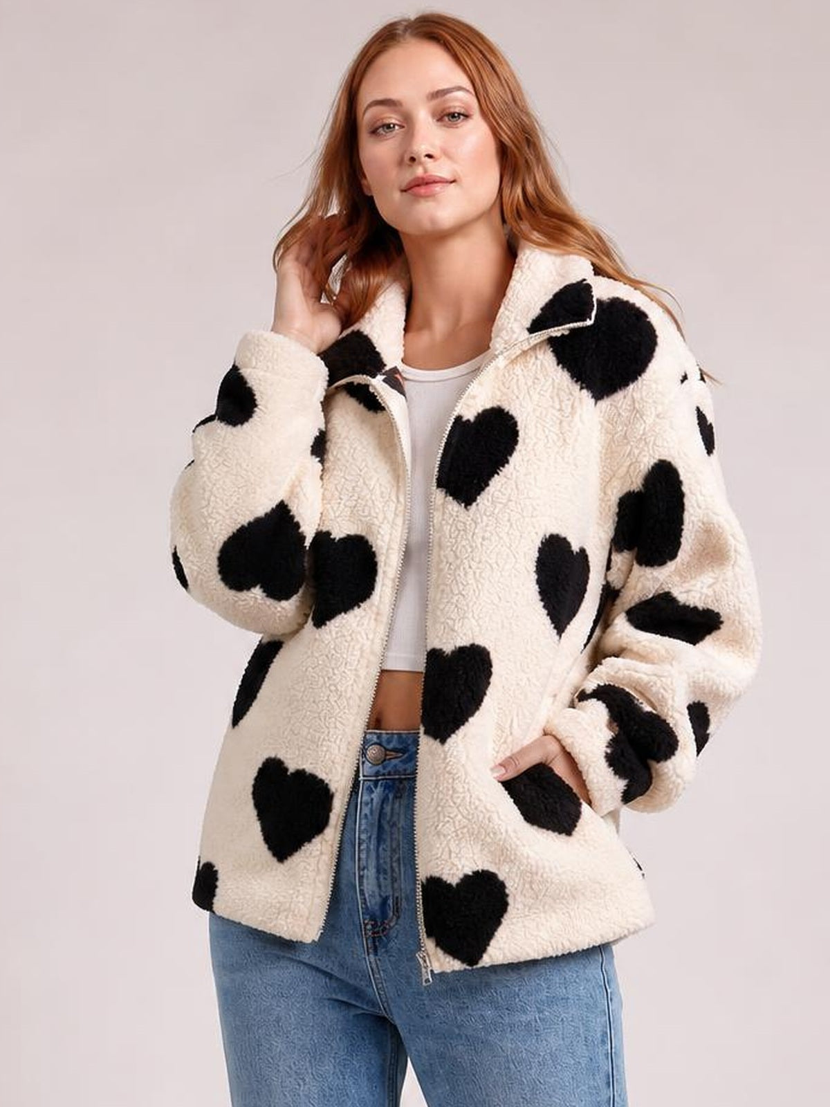 Model wears a cream furry heart jacket with black heart prints, zip-up front, drop shoulders, oversized silhouette, and ribbed cuffs.