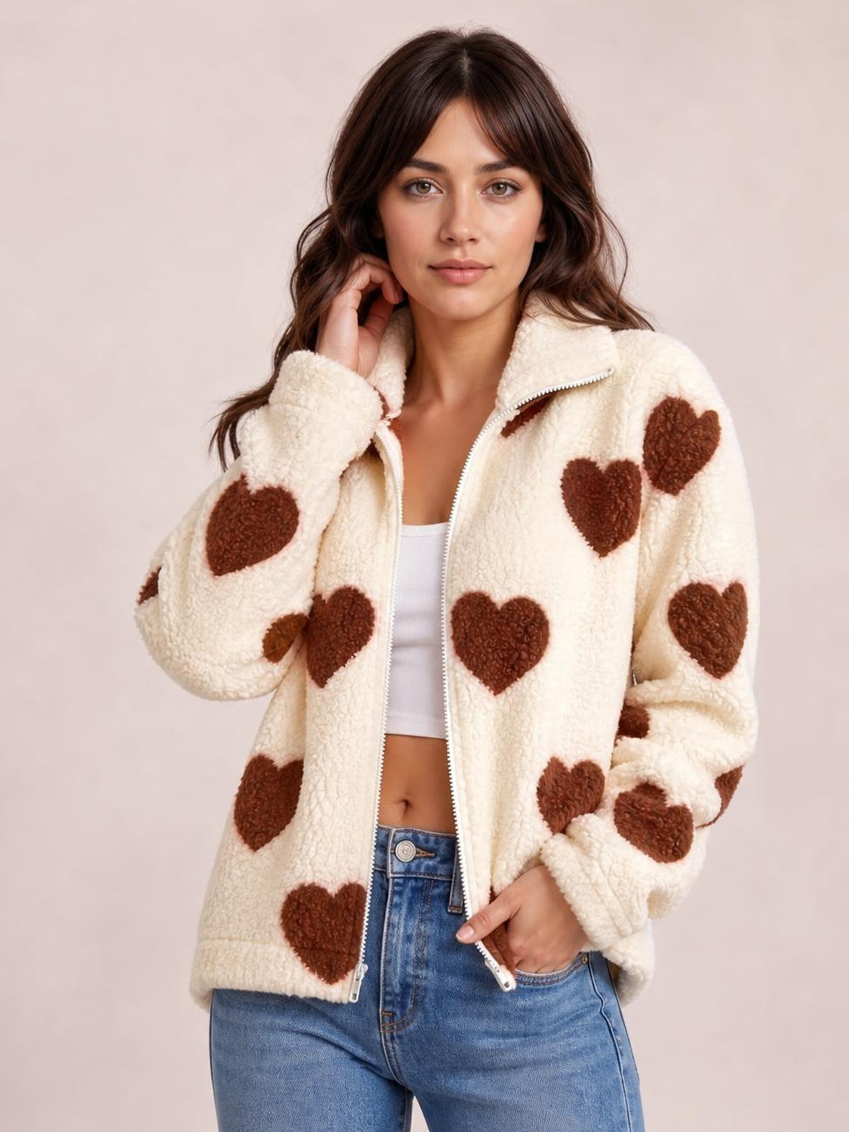 Model poses in an ivory furry heart-print jacket with drop shoulders, a stand collar, and an open front zipper over a white crop top.