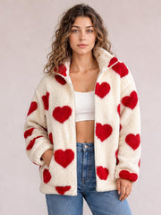 Model wears an off-white furry heart-print jacket with red hearts, drop shoulders, a plush collar, long sleeves, and a front zip closure.