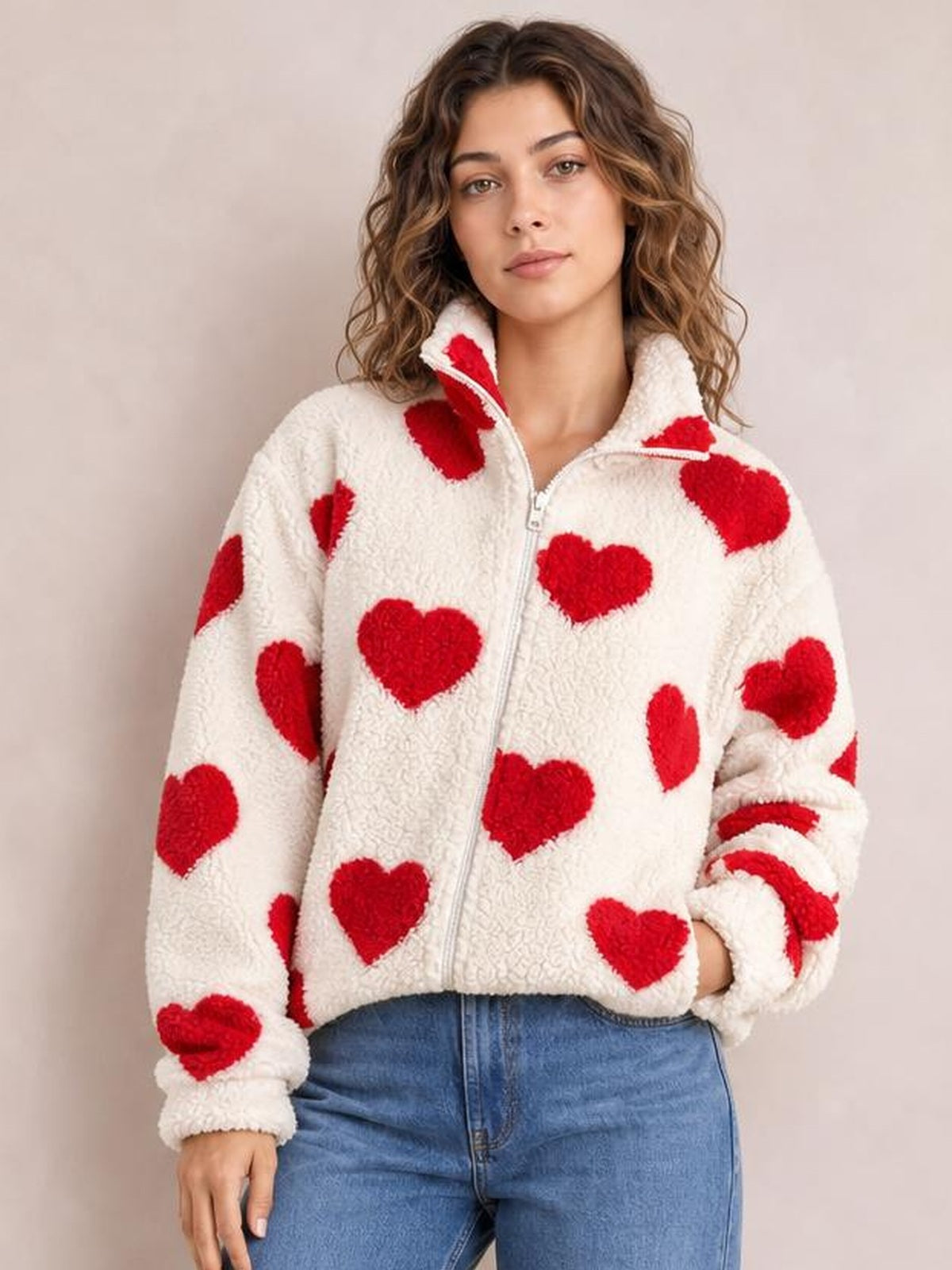 A model poses in a white furry heart jacket with red heart prints, a full zip front, stand collar, drop shoulders, and relaxed silhouette.