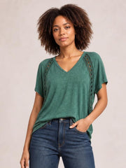 A model poses in a loose heathered green V-neck short sleeve T-shirt with subtle eyelet side details and a relaxed, untucked silhouette.