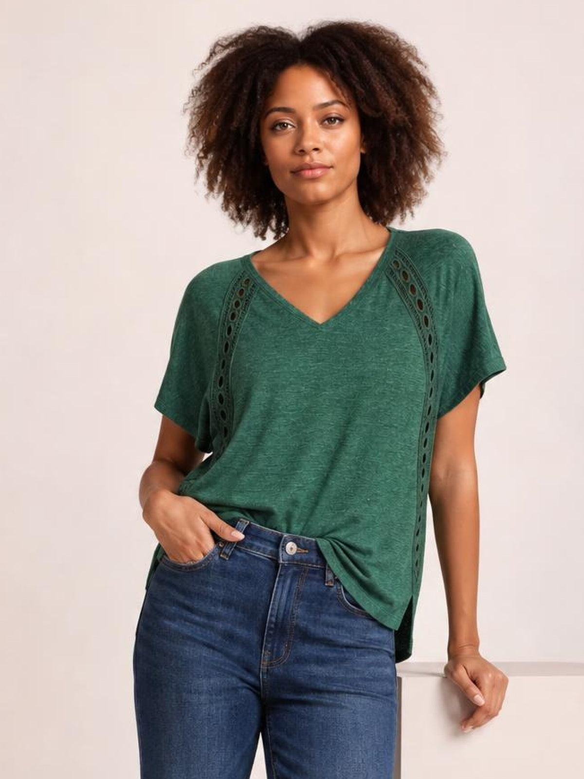 A model poses in a relaxed green heathered V-neck short sleeve T-shirt with a loose silhouette and decorative eyelet panels along the shoulders.