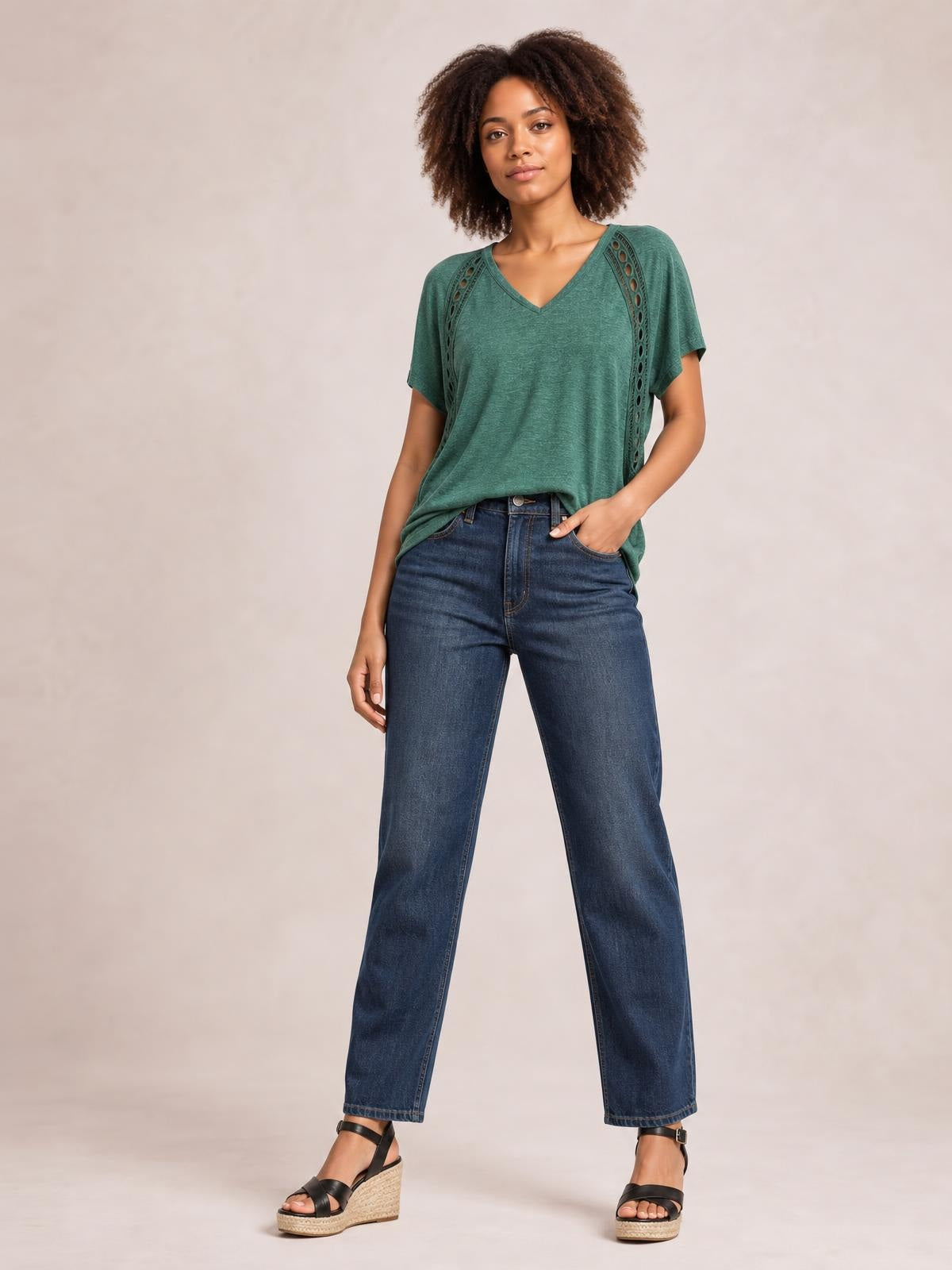 A model poses with one hand in her pocket wearing a heathered green V-neck short sleeve T-shirt with eyelet details and a relaxed silhouette.