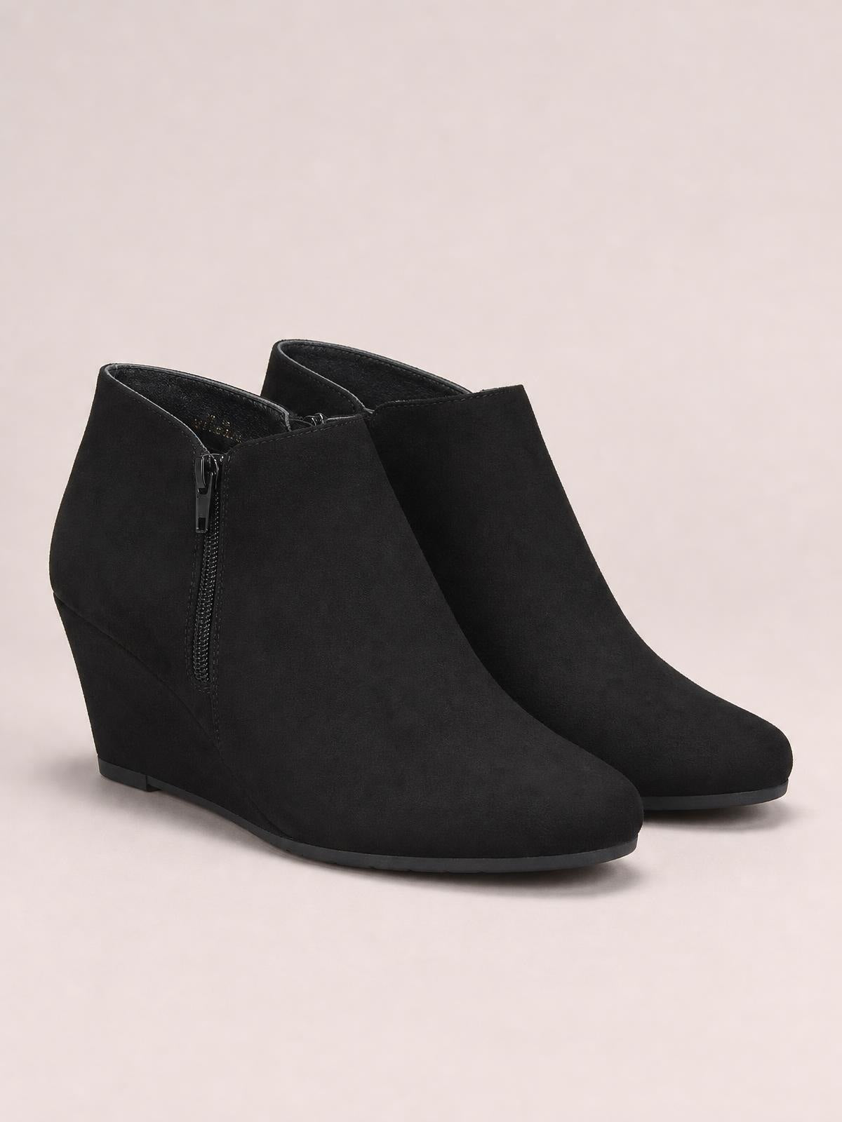 Black suede ankle boots feature a sleek low-cut shaft, side zip closure, rounded toes, high wedge heels, and durable rubber soles.