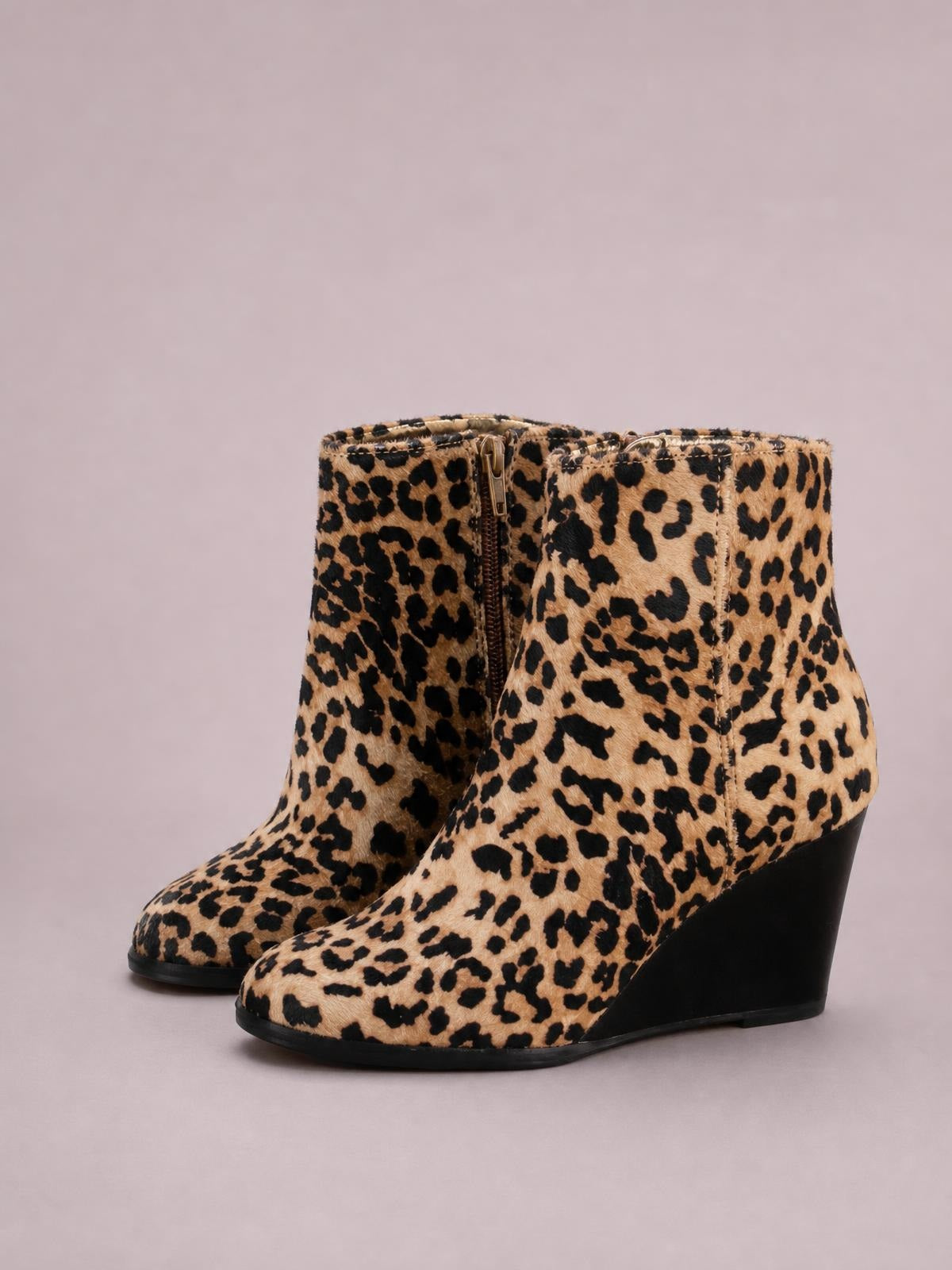 Leopard-print ankle boots in tan and black feature side zips, rounded toes, sleek construction, and high wedge heels in a bold silhouette.