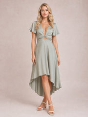 Model stands with crossed legs in a light sage High-Low Plunge Flutter Sleeve Dress featuring a deep neckline, crisscross tied waist, and flowing skirt.