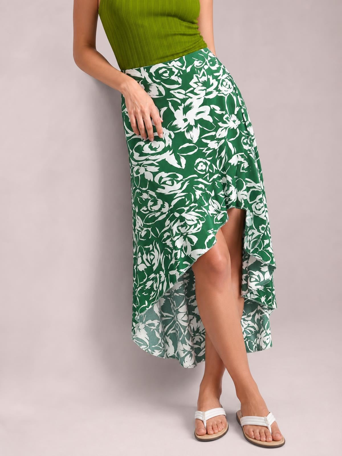 A model poses in a green-and-white floral printed high-waist skirt with a flowing asymmetrical silhouette and dramatic high-low hem.