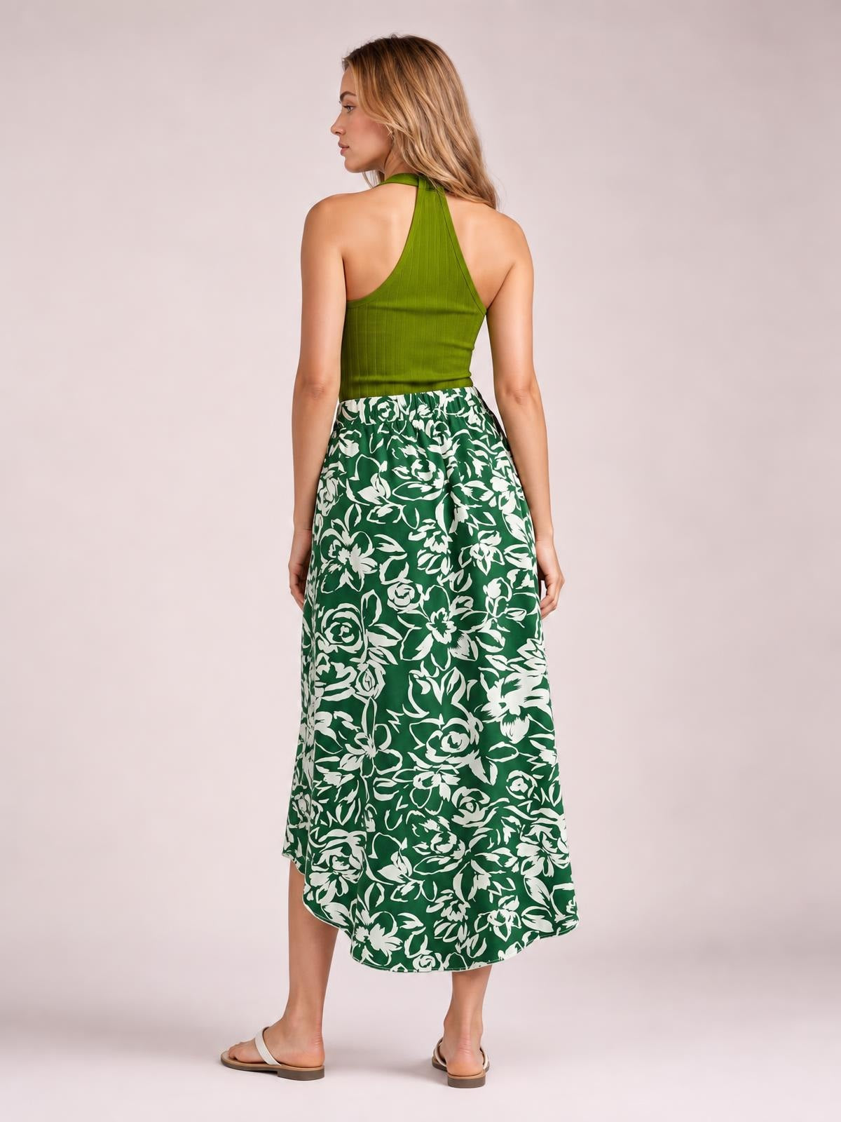 Model shown from behind wears a green and white floral printed high-waist skirt with a flowing asymmetrical high-low hem and relaxed silhouette.