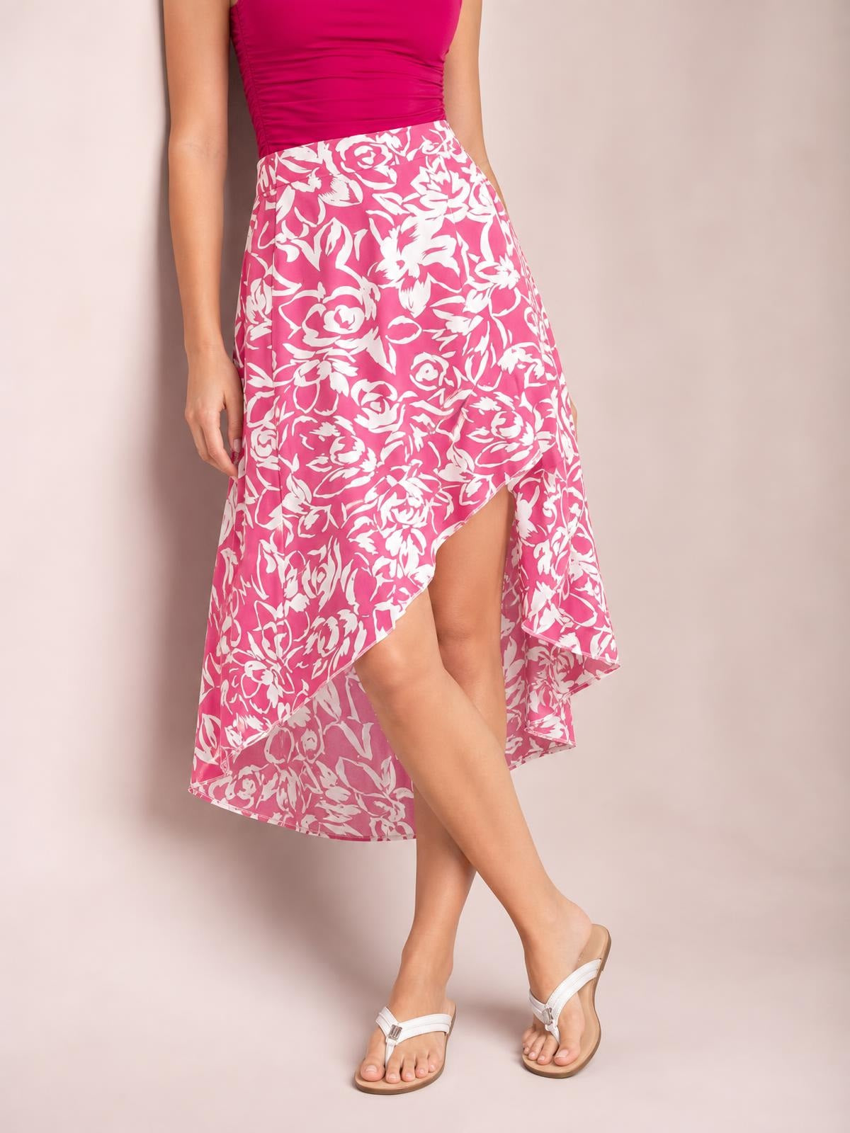 A model poses with crossed legs in a pink floral printed high-waist skirt featuring an asymmetrical silhouette and flowing high-low hem.