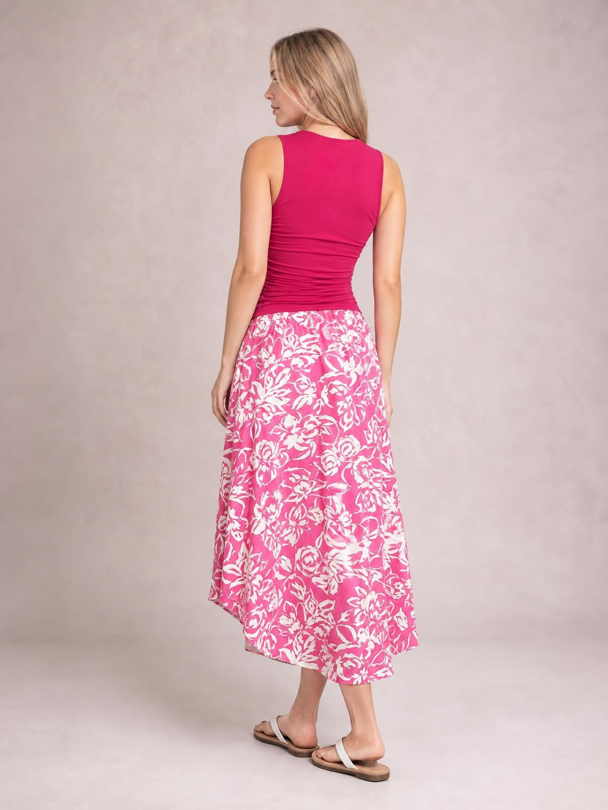 Model shown from behind wearing a pink floral printed high-waist skirt with a flowing asymmetrical high-low hem and feminine A-line silhouette.
