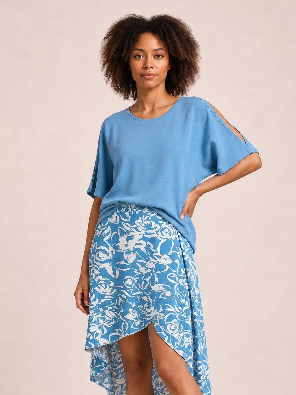 Model poses in a blue and white floral printed high-waist skirt with an asymmetrical high-low hem and draped silhouette.