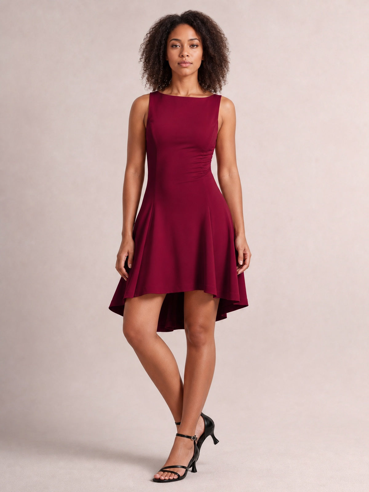 Model poses in a burgundy high-low round neck sleeveless mini dress with a fitted waist, softly flared silhouette, and asymmetric hem.
