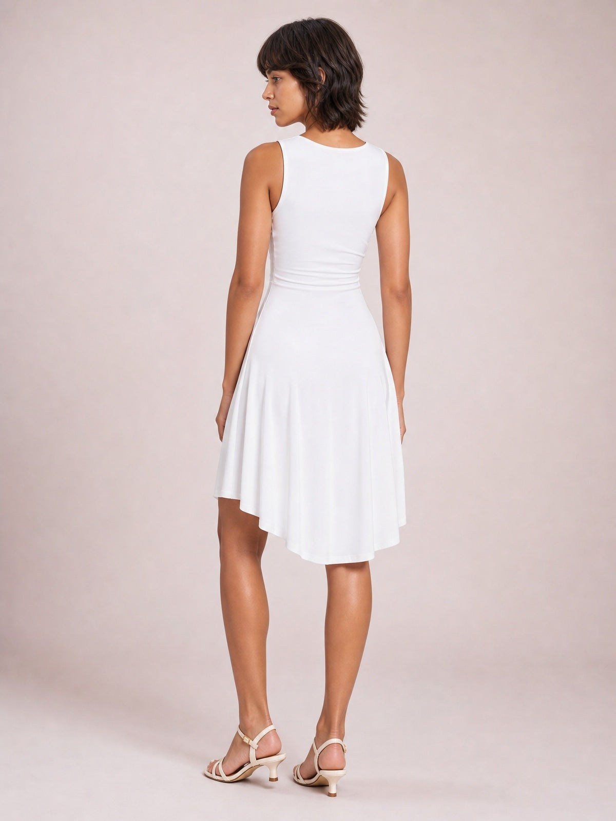 Model in a white high-low round neck sleeveless mini dress, shown from the back with a fitted waist and softly flared skirt.