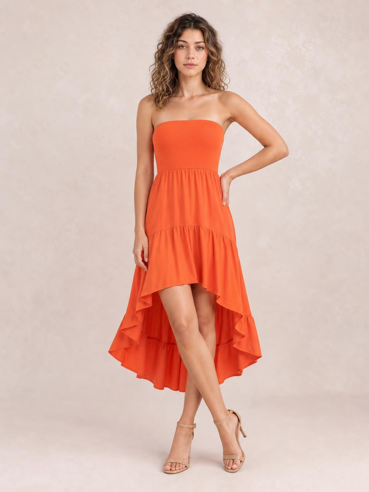 A model poses in an orange strapless tube dress with a gathered waist, tiered ruffles, and a dramatic high-low hem.