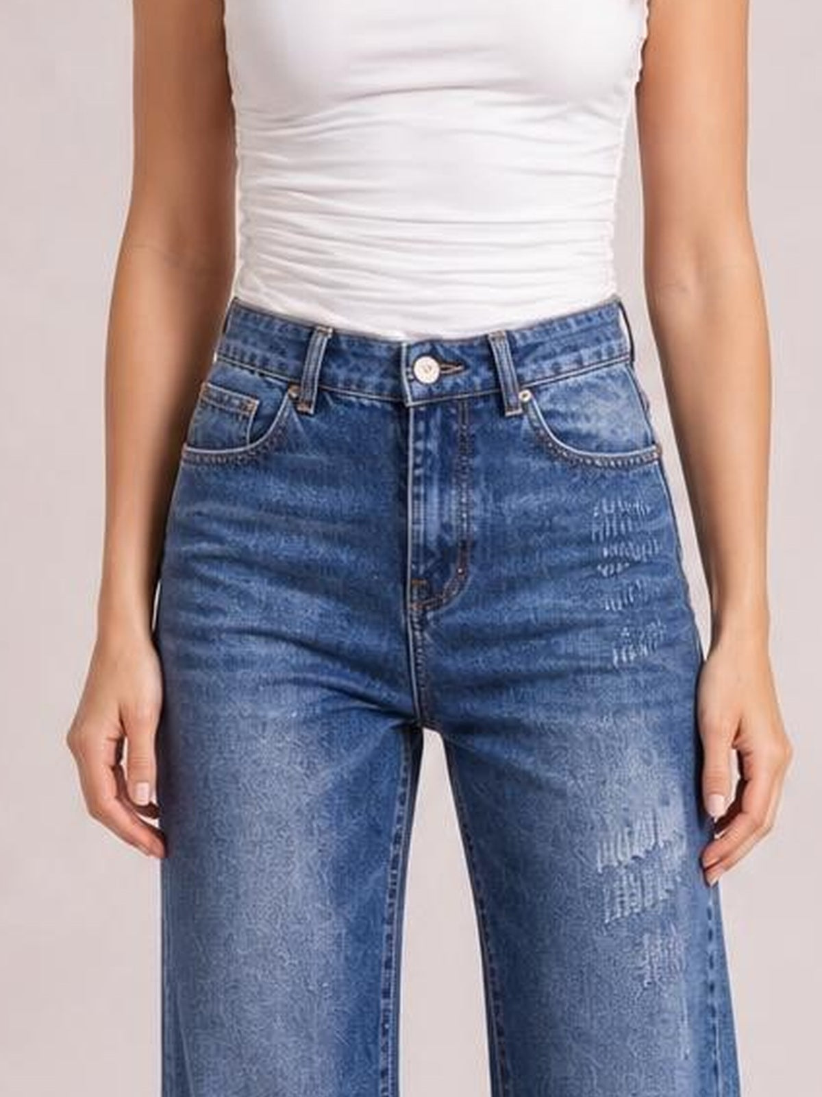 Model standing with hands at her sides, wearing blue high-rise bootcut jeans with front pockets, belt loops, button closure, and a fitted waist.