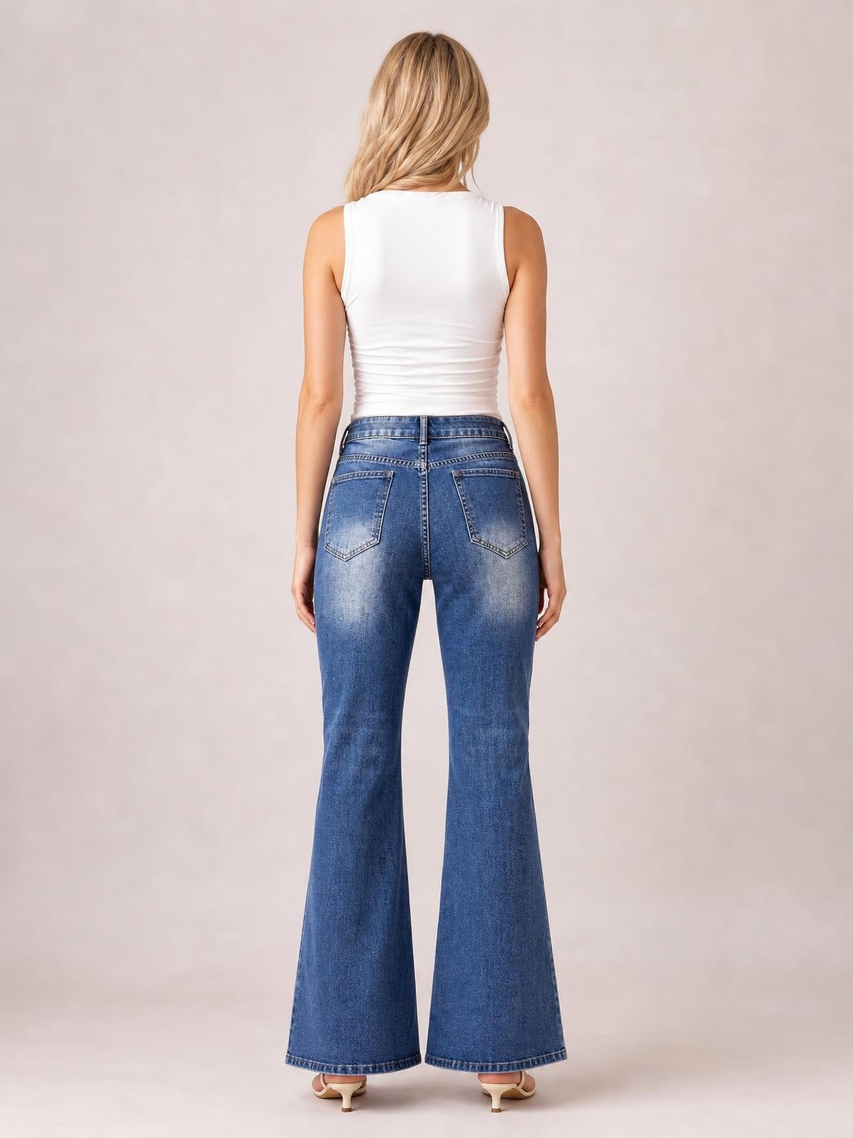 Model shown from the back in high-rise blue bootcut jeans with button closure, belt loops, contrast stitching, and two back pockets.