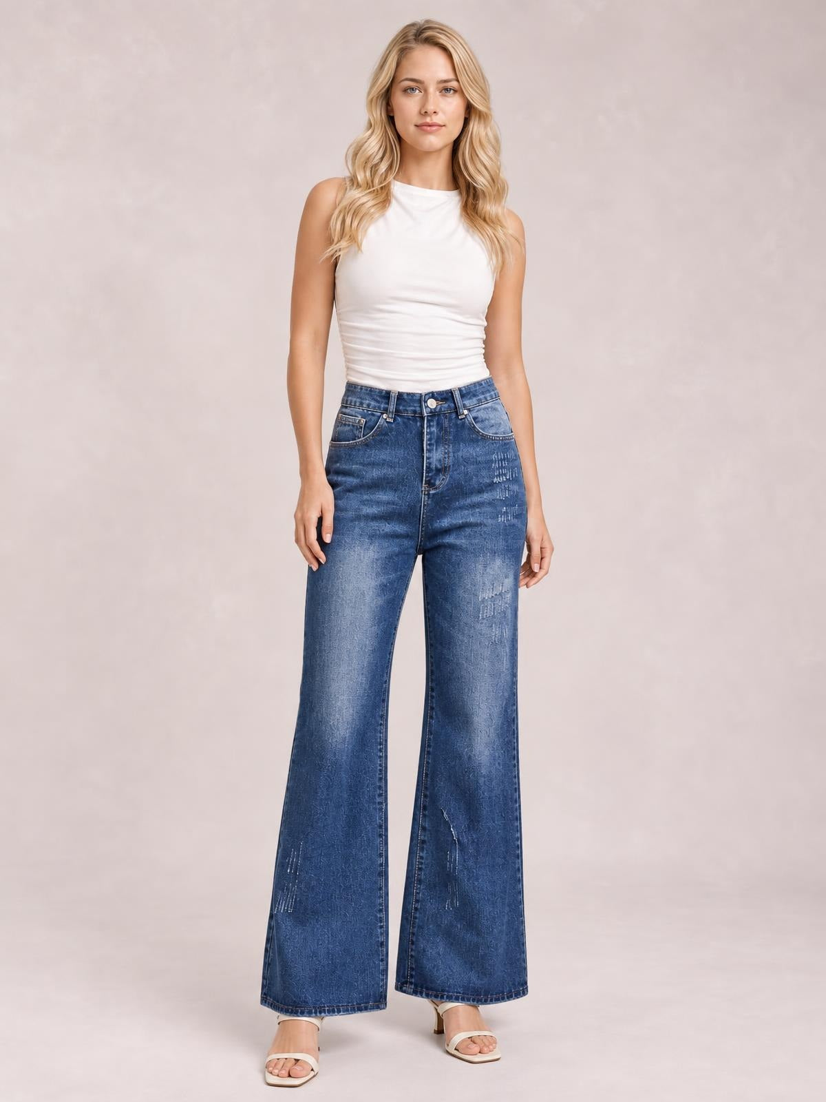 A model stands facing forward in blue high-rise bootcut jeans with front pockets, button closure, contrast fading, and a relaxed full-length silhouette.