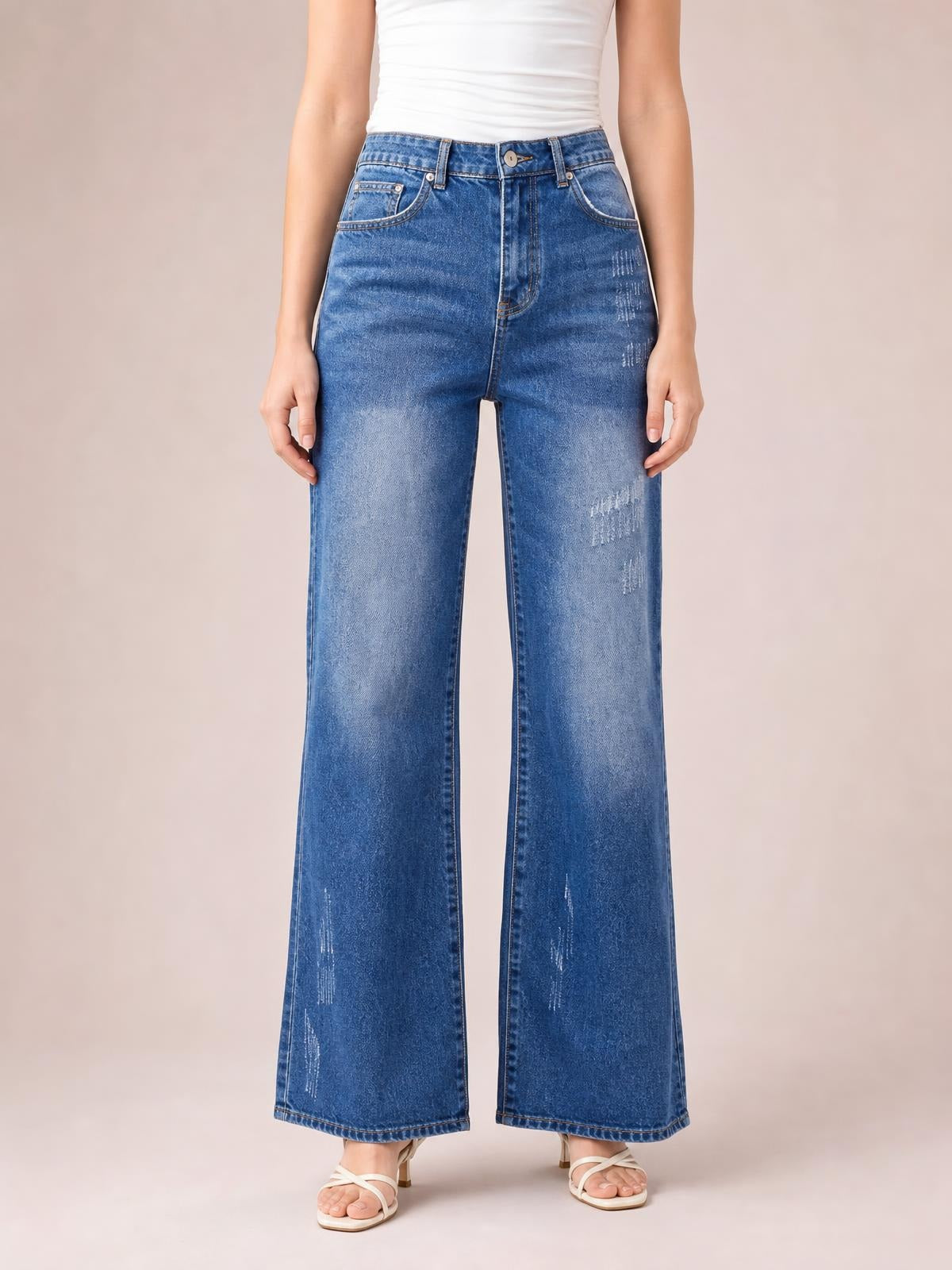 Model stands facing forward in blue high-rise bootcut jeans with front pockets, button closure, belt loops, faded detailing, and wide hems.
