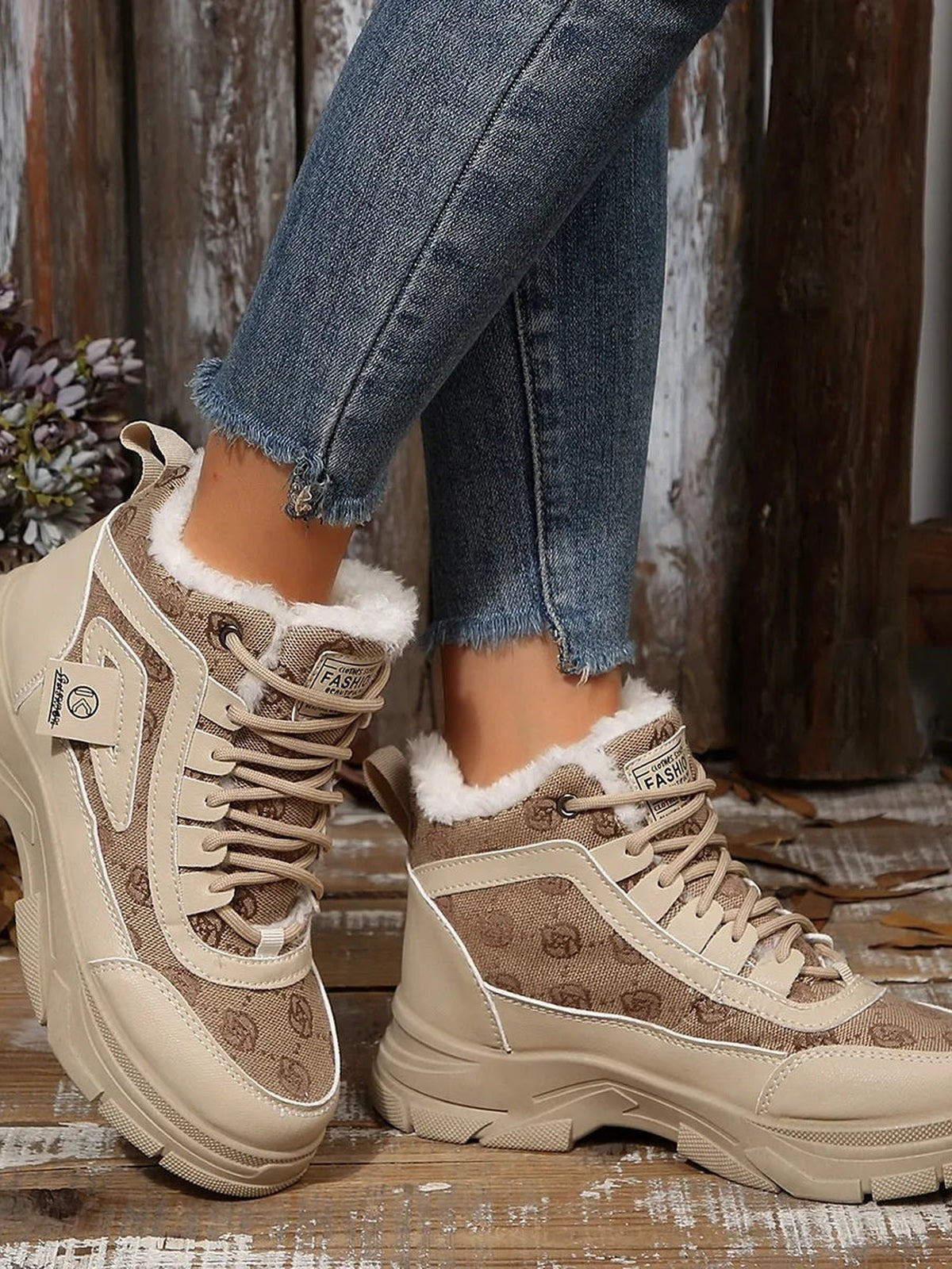 Model crosses her legs to showcase beige high-top platform chunky sneaker boots with lace-up fronts, fluffy collars, layered panels, and thick sculpted soles.