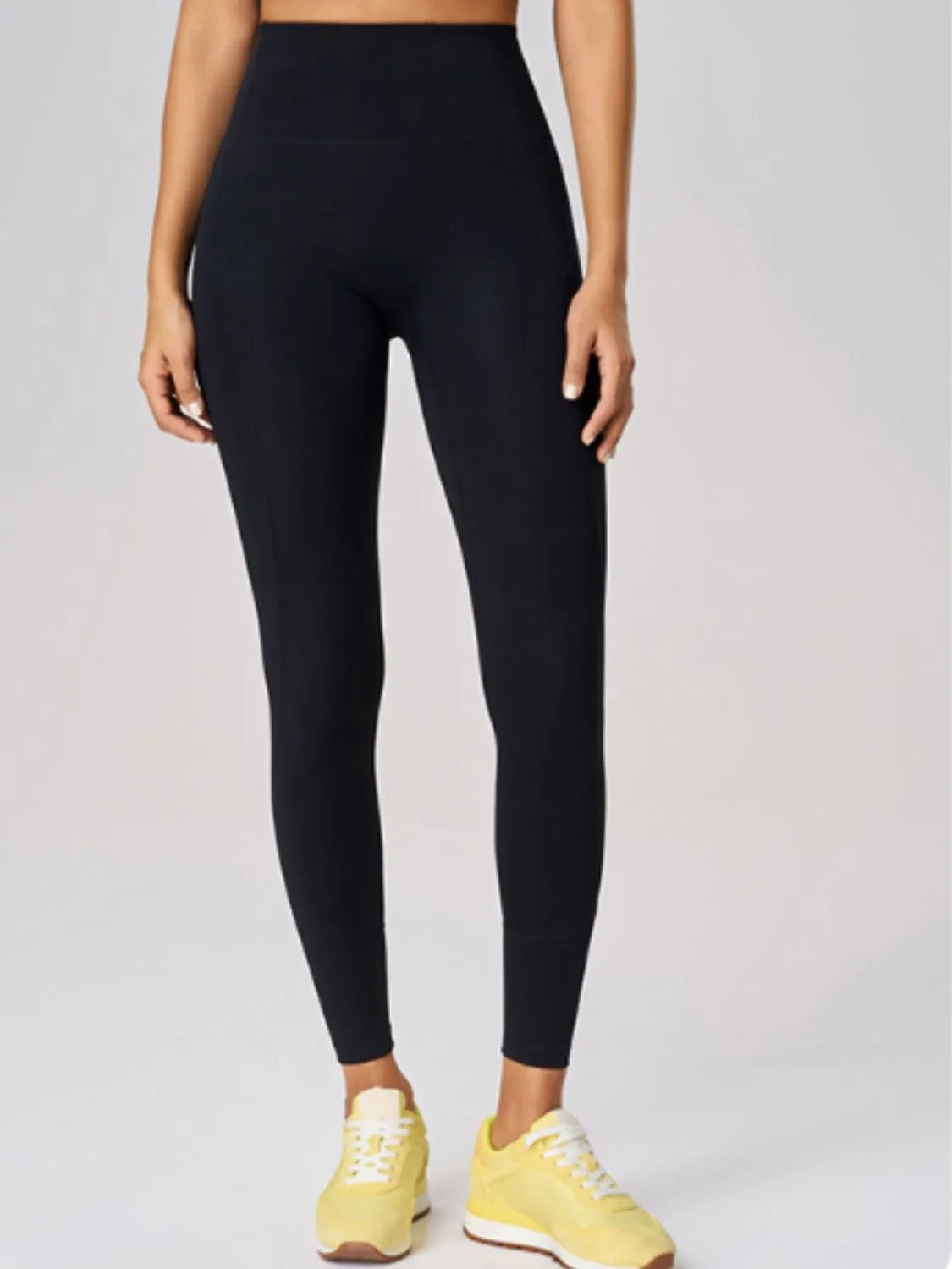 Model wearing black high waist active leggings with a smooth, close-fitting silhouette and ankle-length tapered legs, standing with hands at her sides.