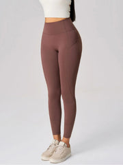 A model stands in brown high-waist active leggings with a fitted ankle-length silhouette, moderate stretch, and visible side pocket and panel seams.