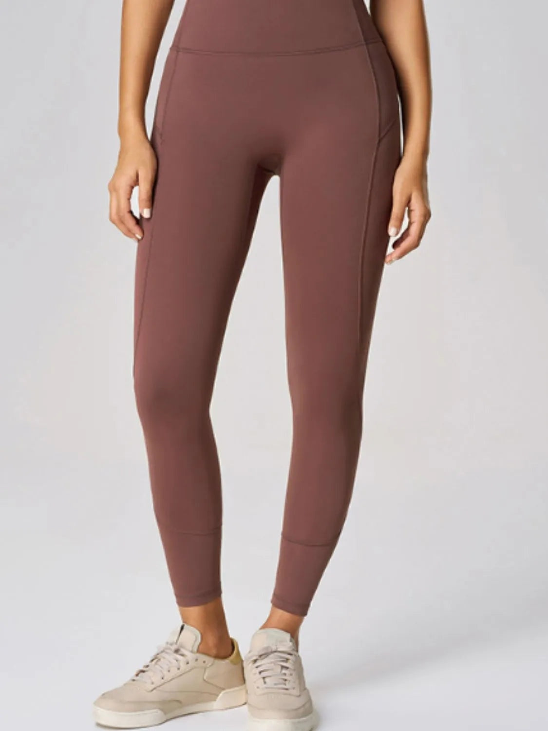 Model wearing high waist brown active leggings with a smooth, fitted silhouette, seamed waistband, and tapered ankle-length construction.