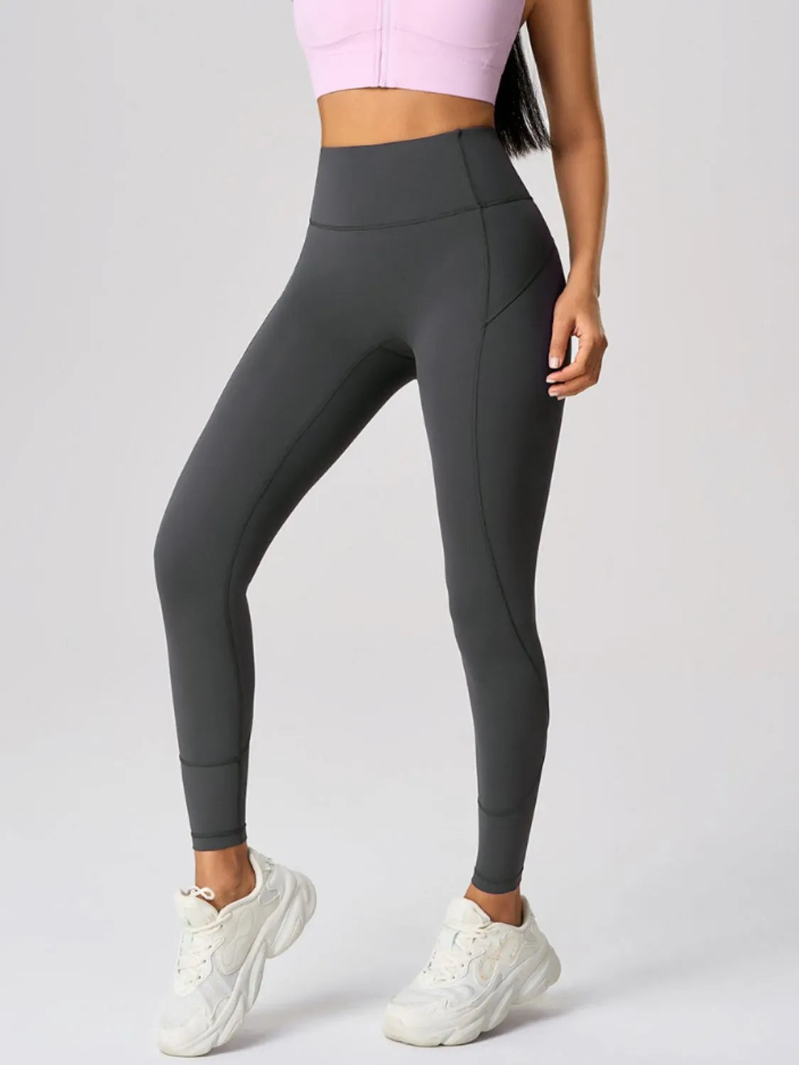 Model wearing dark gray high waist active leggings with a wide waistband, sleek fitted silhouette, curved seam construction, and a side pocket.