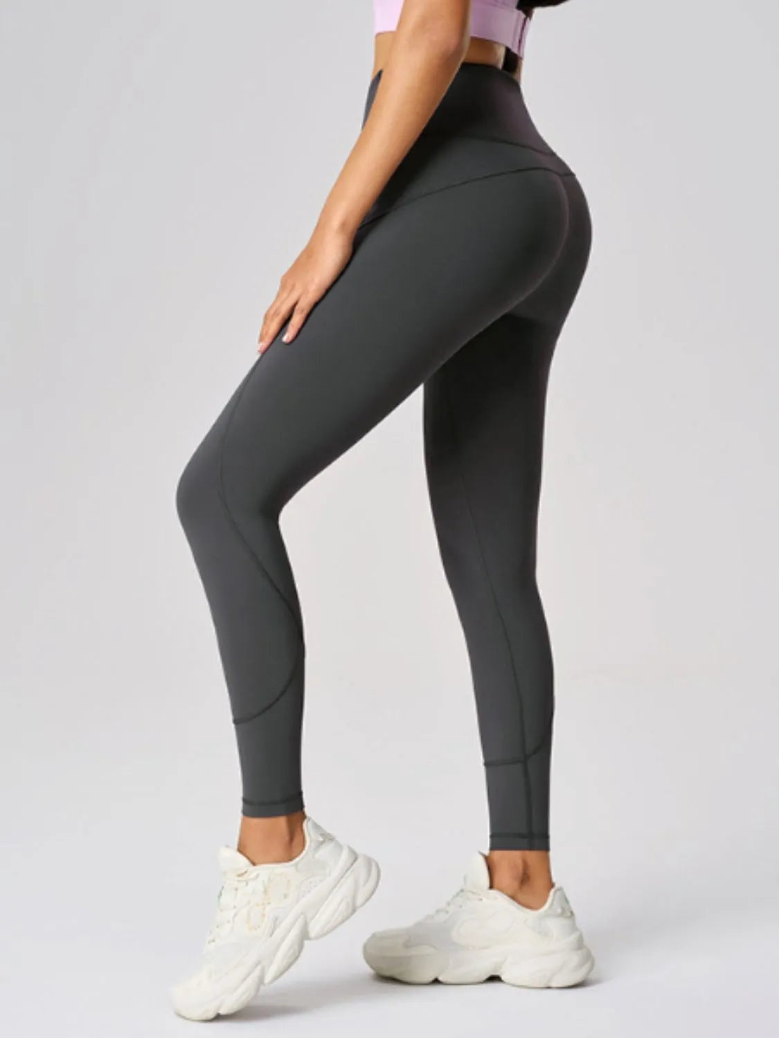 A model poses in black high waist active leggings with a sleek, full-length fitted silhouette, curved seam construction, and one leg bent forward.